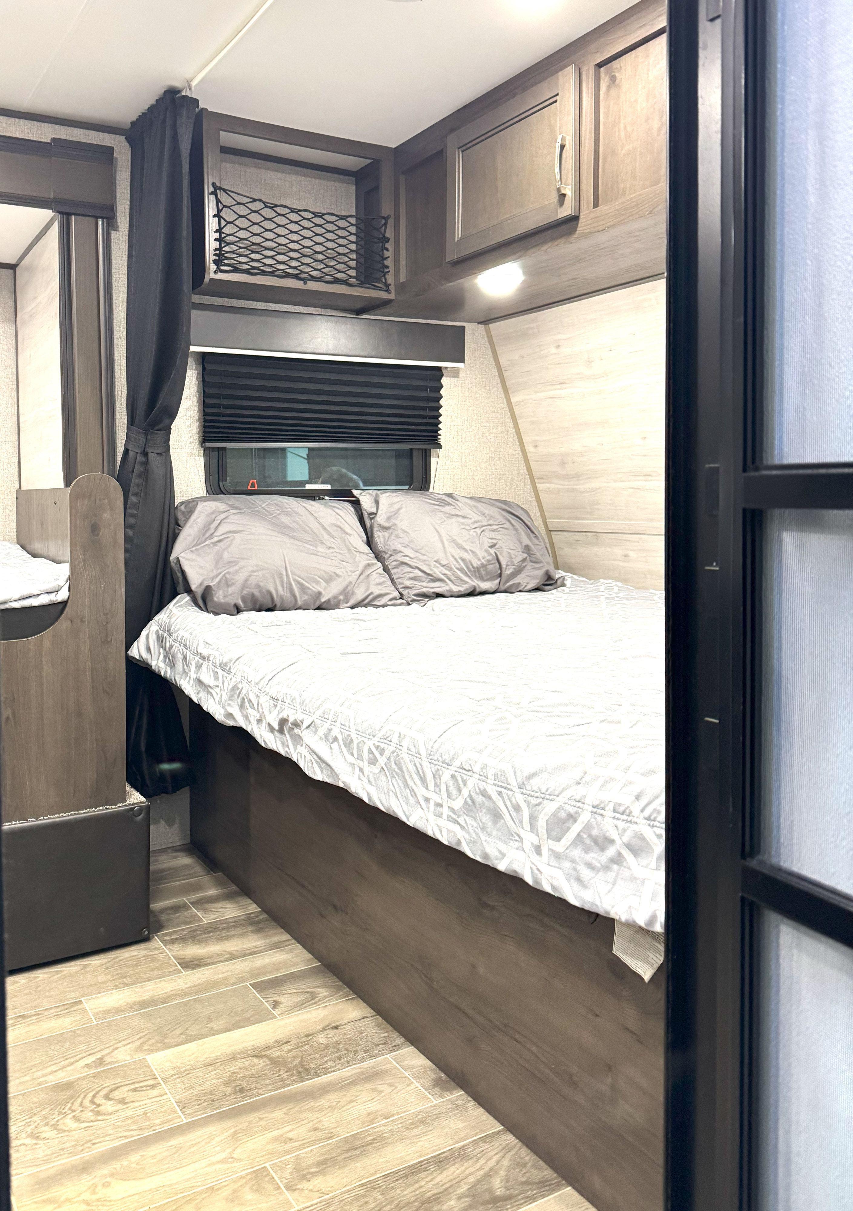RV rental bedroom: Cozy space with a bed, grey pillows, window, overhead cabinets, and dark divider curtain.. Jayco Jay Flight SLX7 184BS 2021