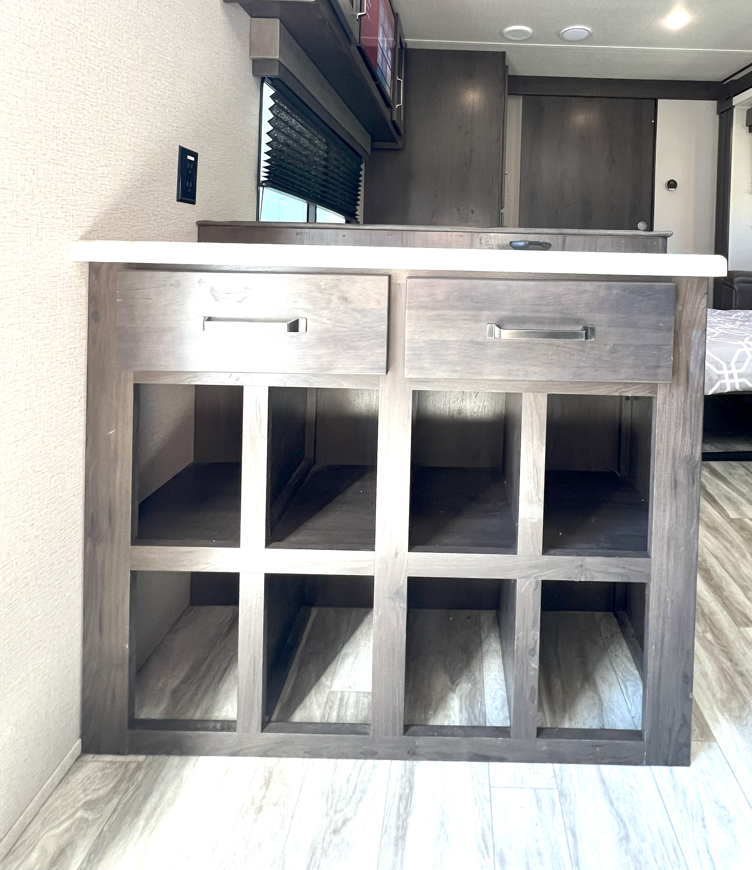 Modern RV rental interior with a grey wooden island featuring two drawers and open cubbies, white counter, and light wood flooring.. Grand Design Transcend Xplor 297QB 2021