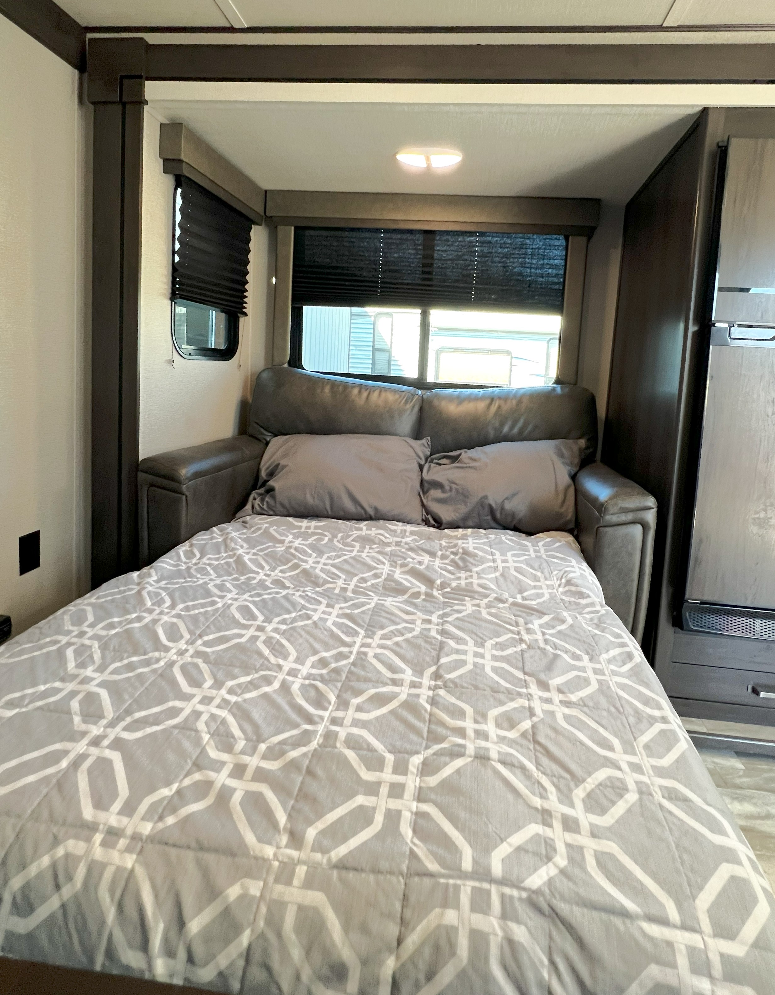 Cozy RV rental interior with a pull-out sofa bed, complete with gray pillows & geometric comforter. Windows have dark blinds.. Grand Design Transcend Xplor 297QB 2021