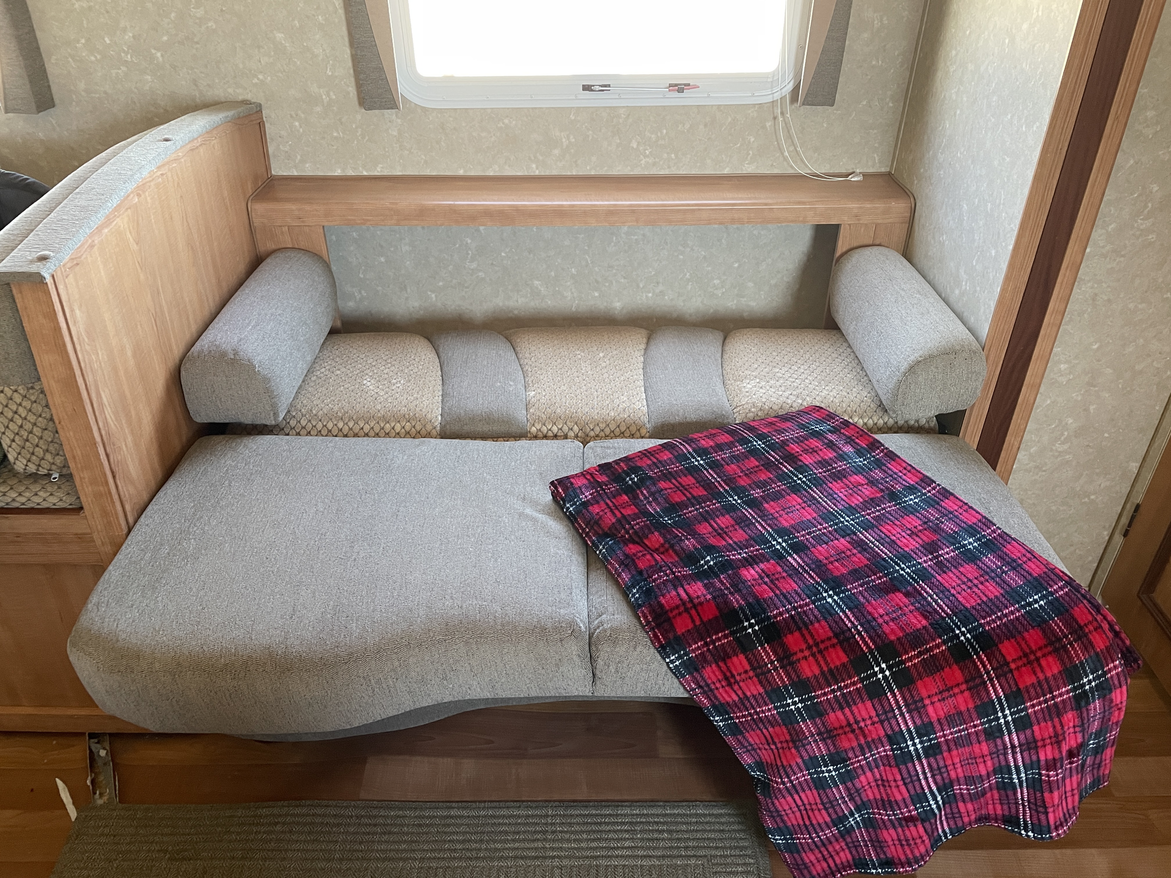 Cozy RV rental interior: Light gray seating/bed area with a red plaid blanket, wood accents, and window.. Gulf Stream Conquest 2011