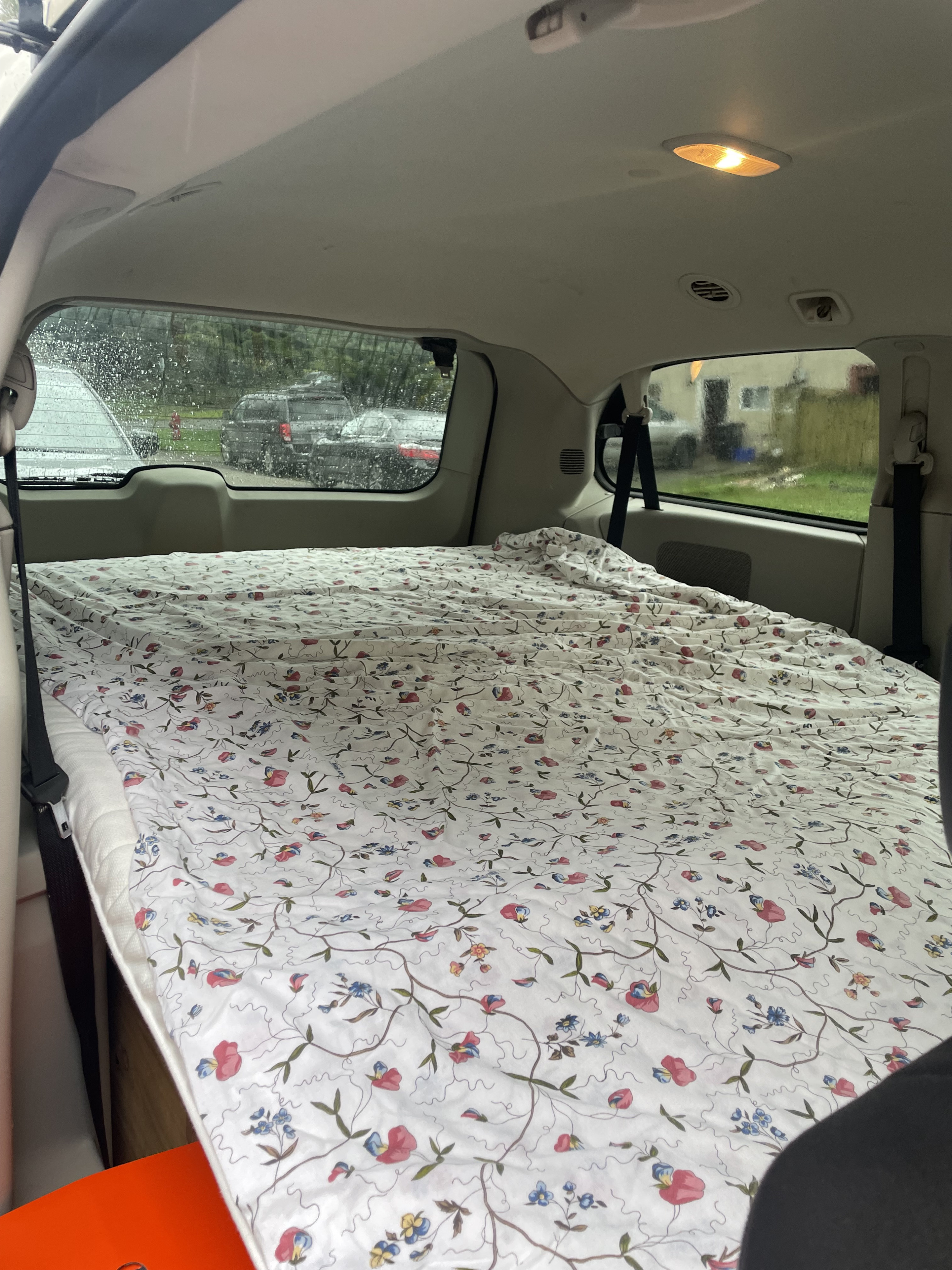 Cozy floral bed setup inside this RV rental offers comfortable car camping. Vehicle interior, with rainy outside view.. Dodge Grand Caravan 2011