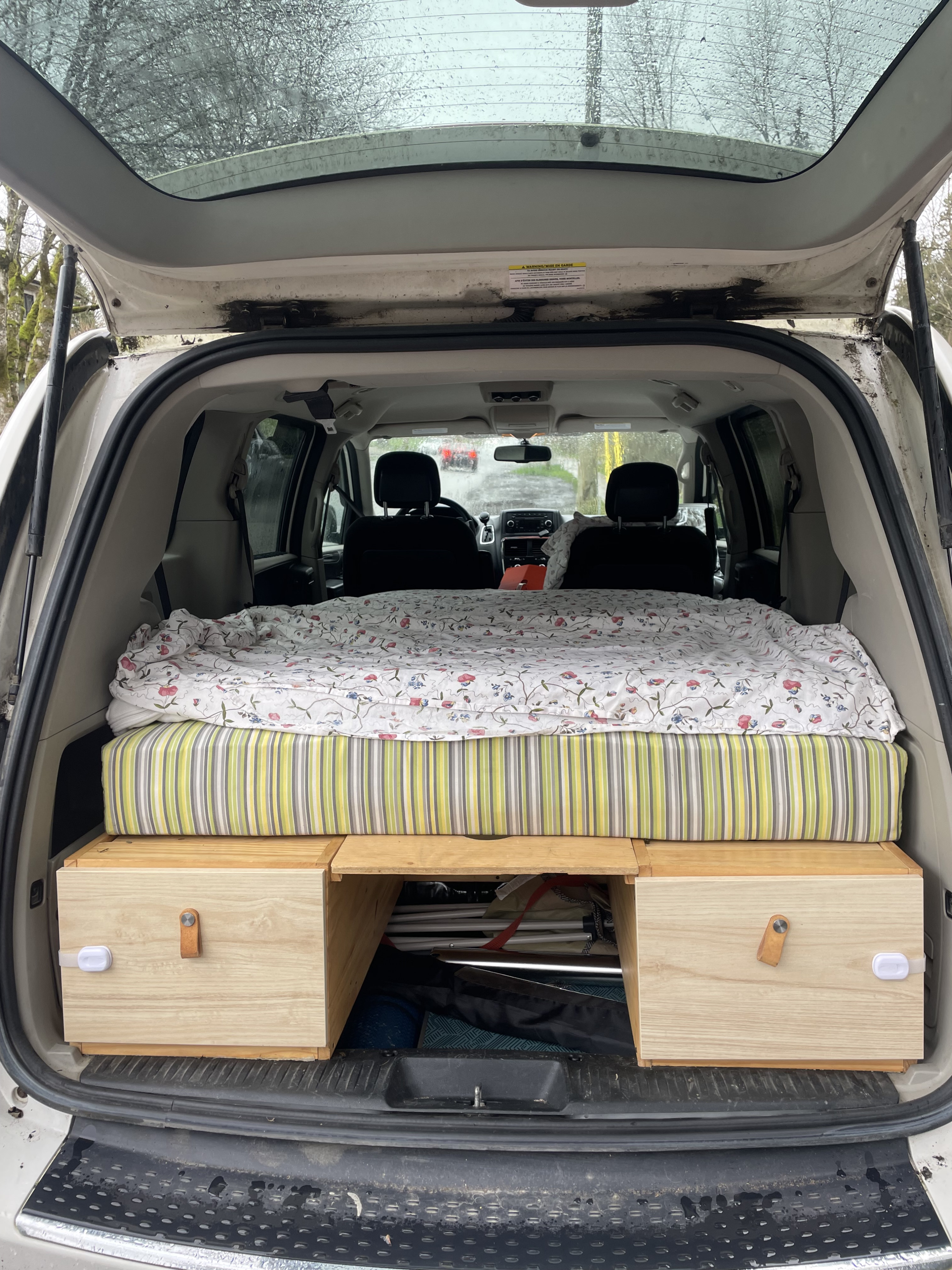 View from the rear of a white minivan, showing a custom bed and storage built for RV rental camping.. Dodge Grand Caravan 2011