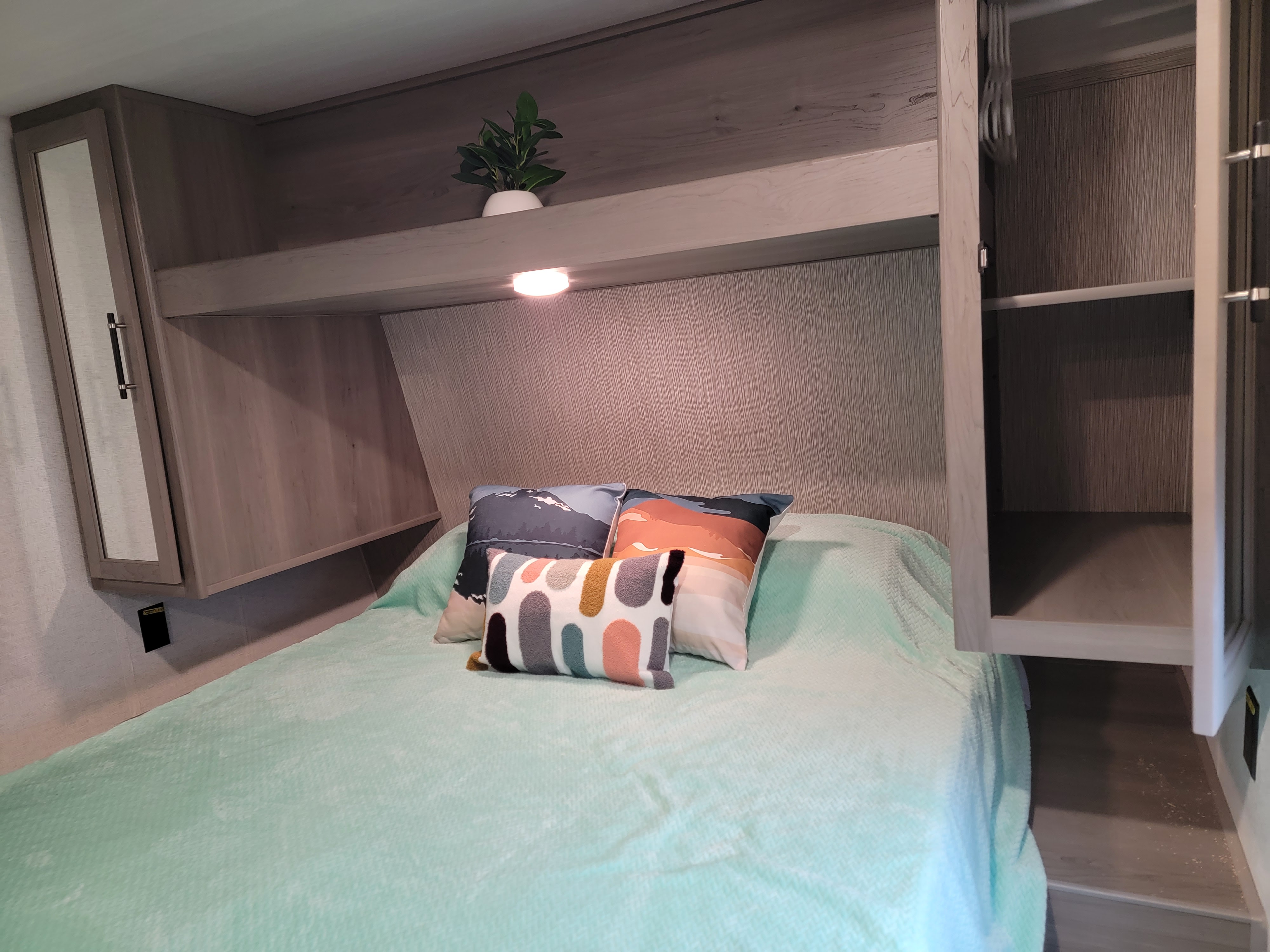 Cozy RV rental bedroom featuring a mint-colored bed with patterned pillows, overhead storage, and built-in cabinets for comfortable travel.. Keystone 261BH 2025