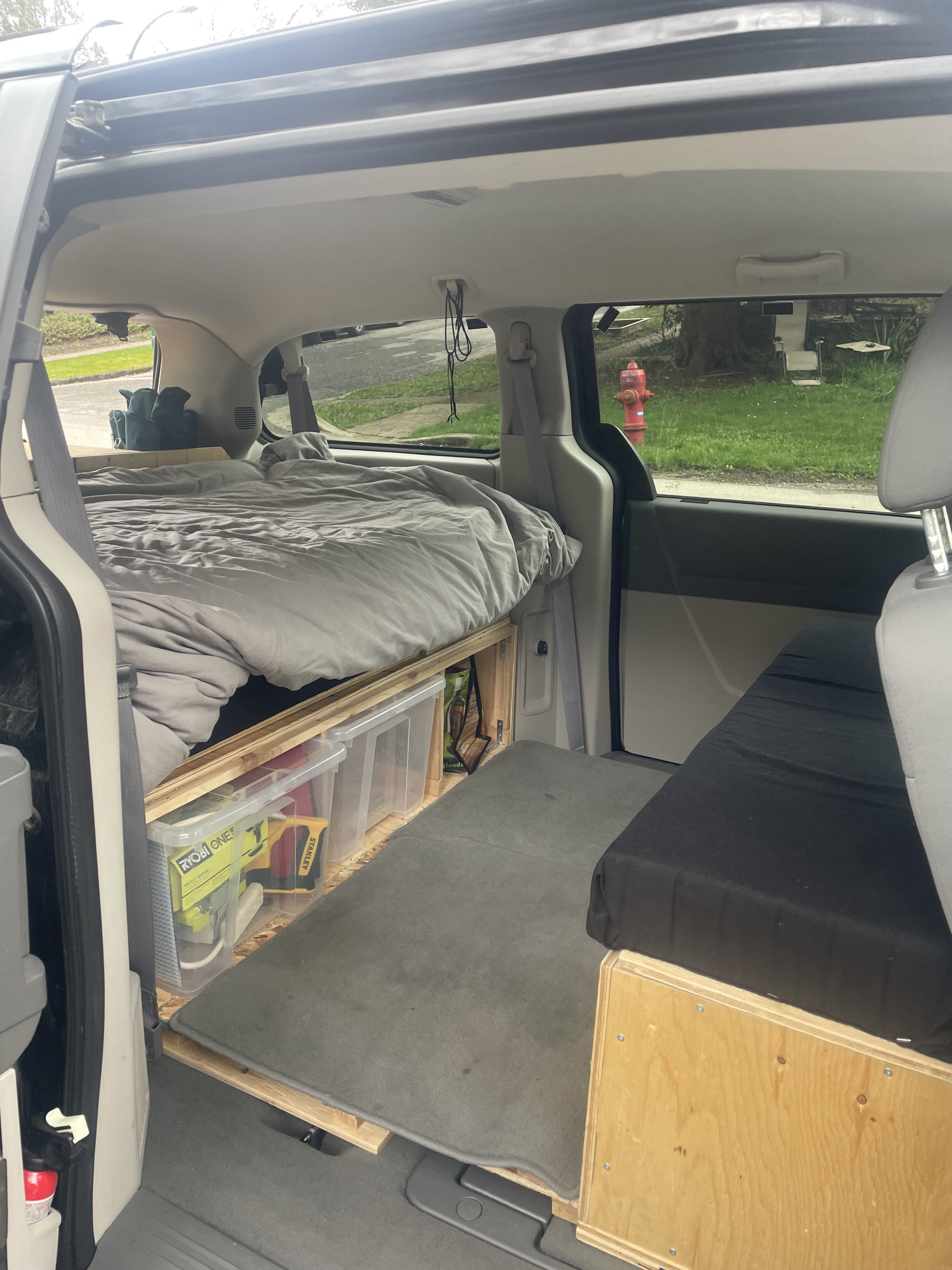 Inside a custom minivan RV rental: features a cozy bed, under-bed tool storage, and a built-in bench for travel.. Dodge Grand Caravan 2009