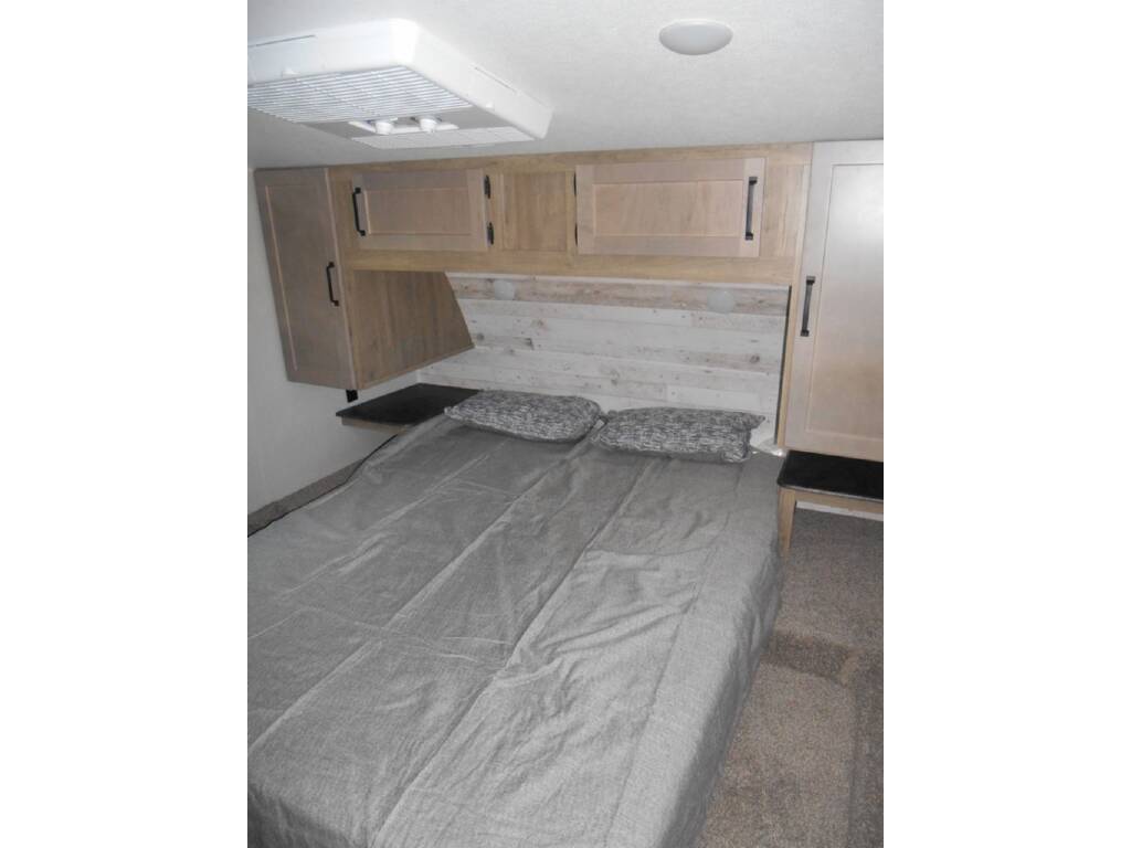 RV rental bedroom features a comfy bed with gray linens, overhead cabinets, and side storage.. Forest River Palomino Puma 2024