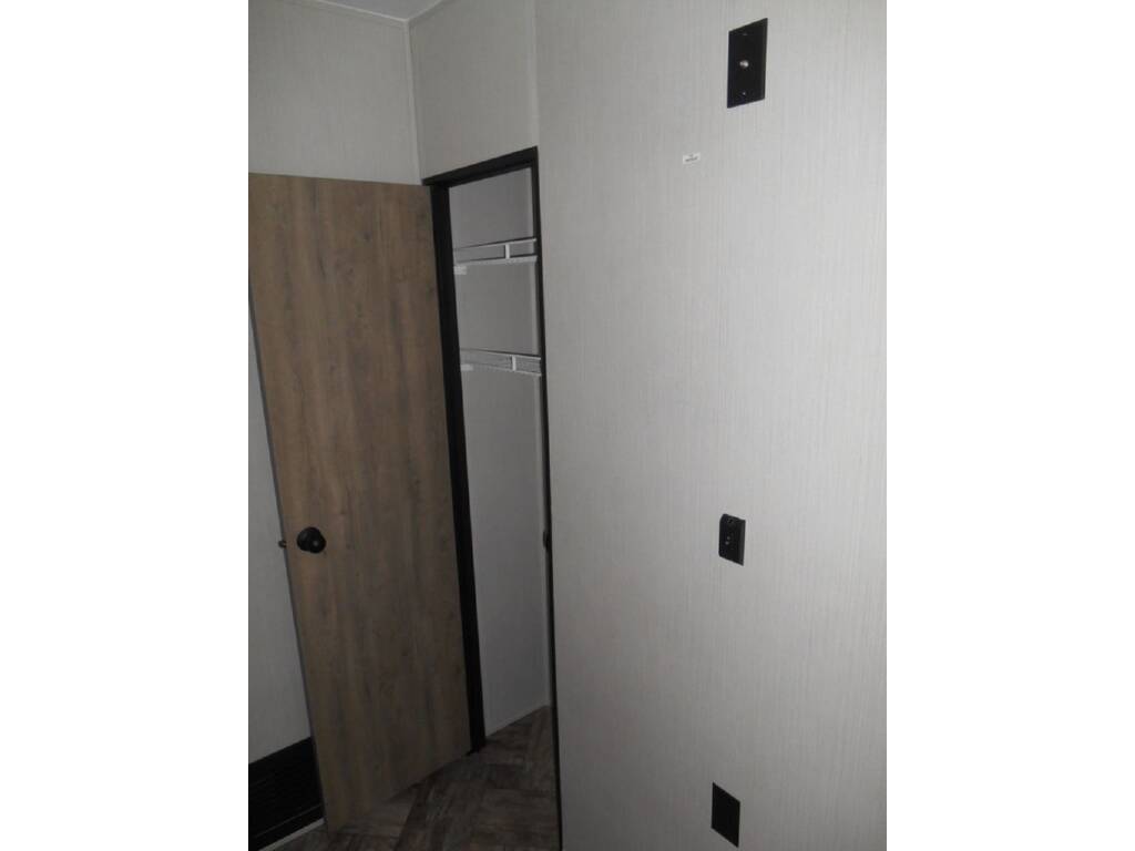 RV rental interior: Wooden door to closet with wire shelves. Light wall has electrical outlets/mounts, showing practical camper space.. Forest River Palomino Puma 2024