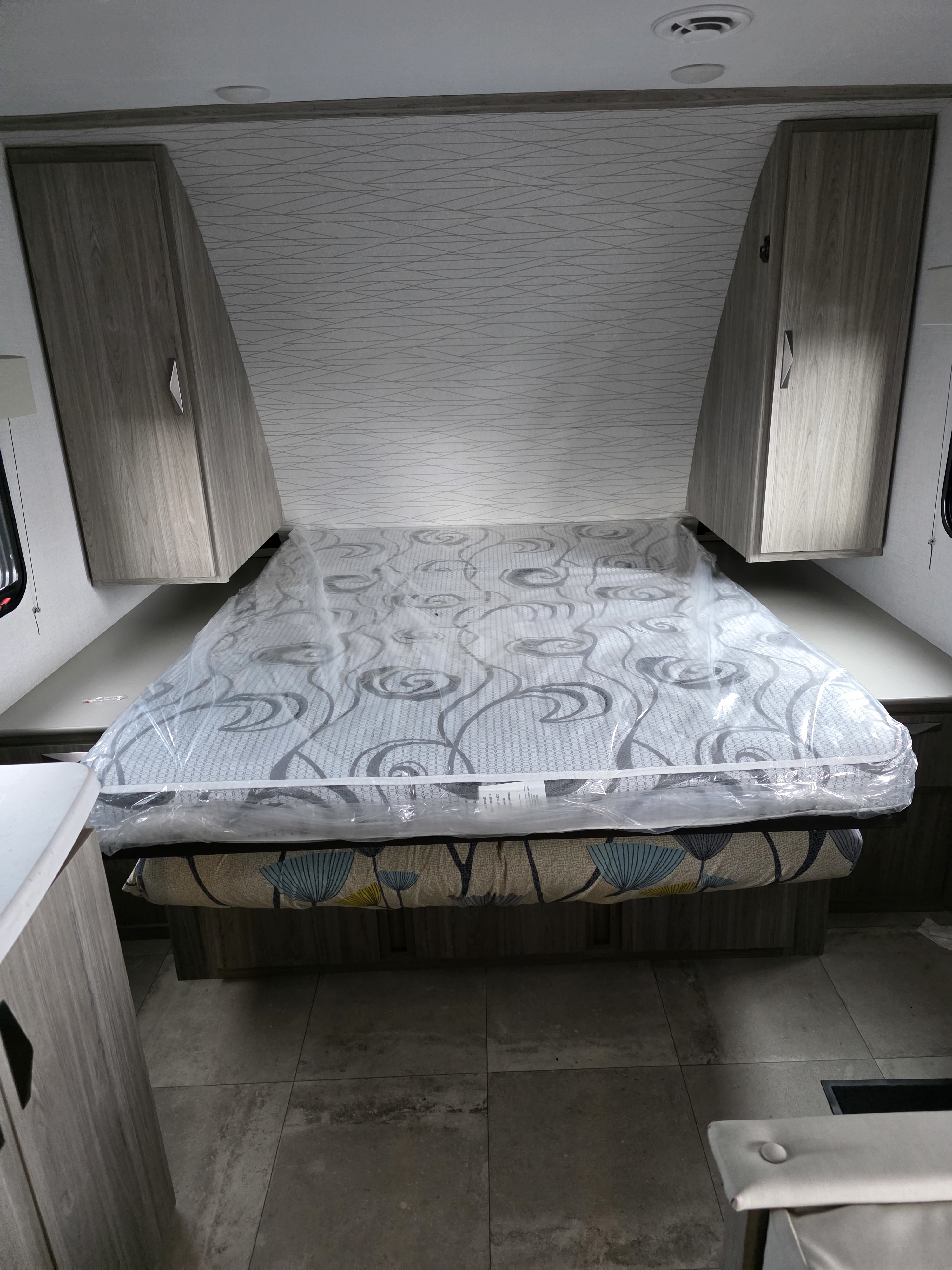 Spacious RV rental bedroom with a new mattress, overhead cabinets, and stylish patterned walls, ready for adventure.. Keystone RV Passport SL Ultra Lite 2024