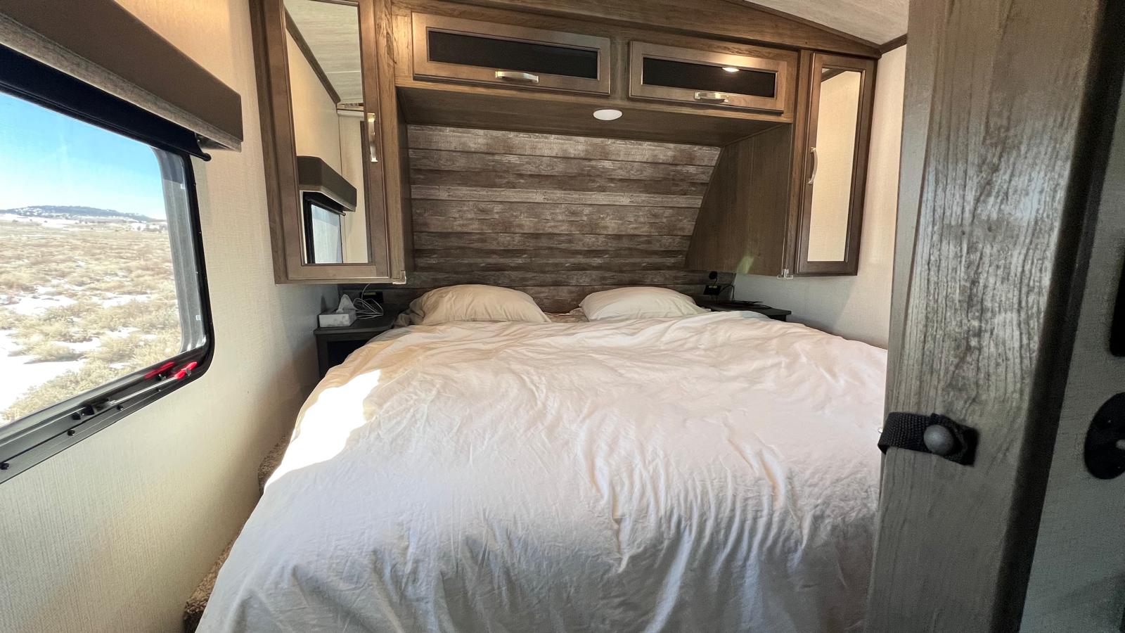Cozy RV rental bedroom with a large bed, overhead storage, and window showing a dry, wintry landscape.. Keystone RV Cougar 2023