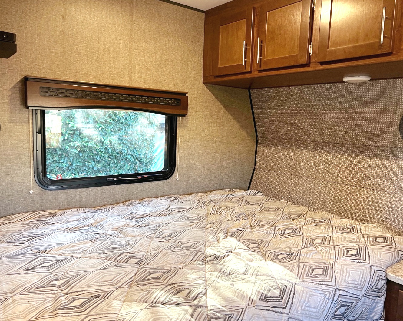 This RV rental bedroom offers a comfortable bed, window for views, and convenient overhead storage cabinets.. Heartland Terry Classic V21 2018