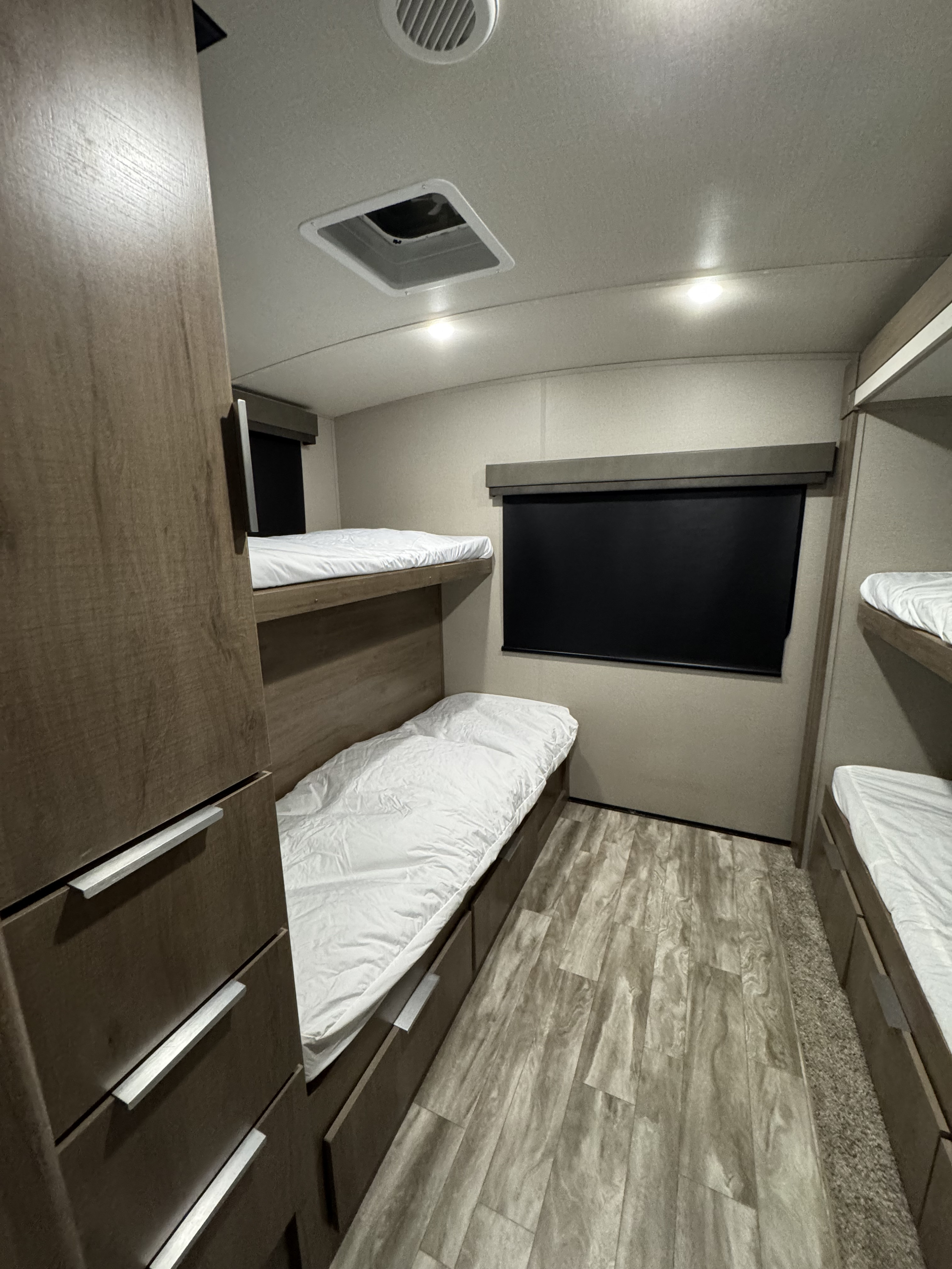 RV rental bunkhouse with two levels of sleeping space, modern wood-look flooring, and a cabinet. Brightly lit RV interior.. Grand Design Imagine 2021