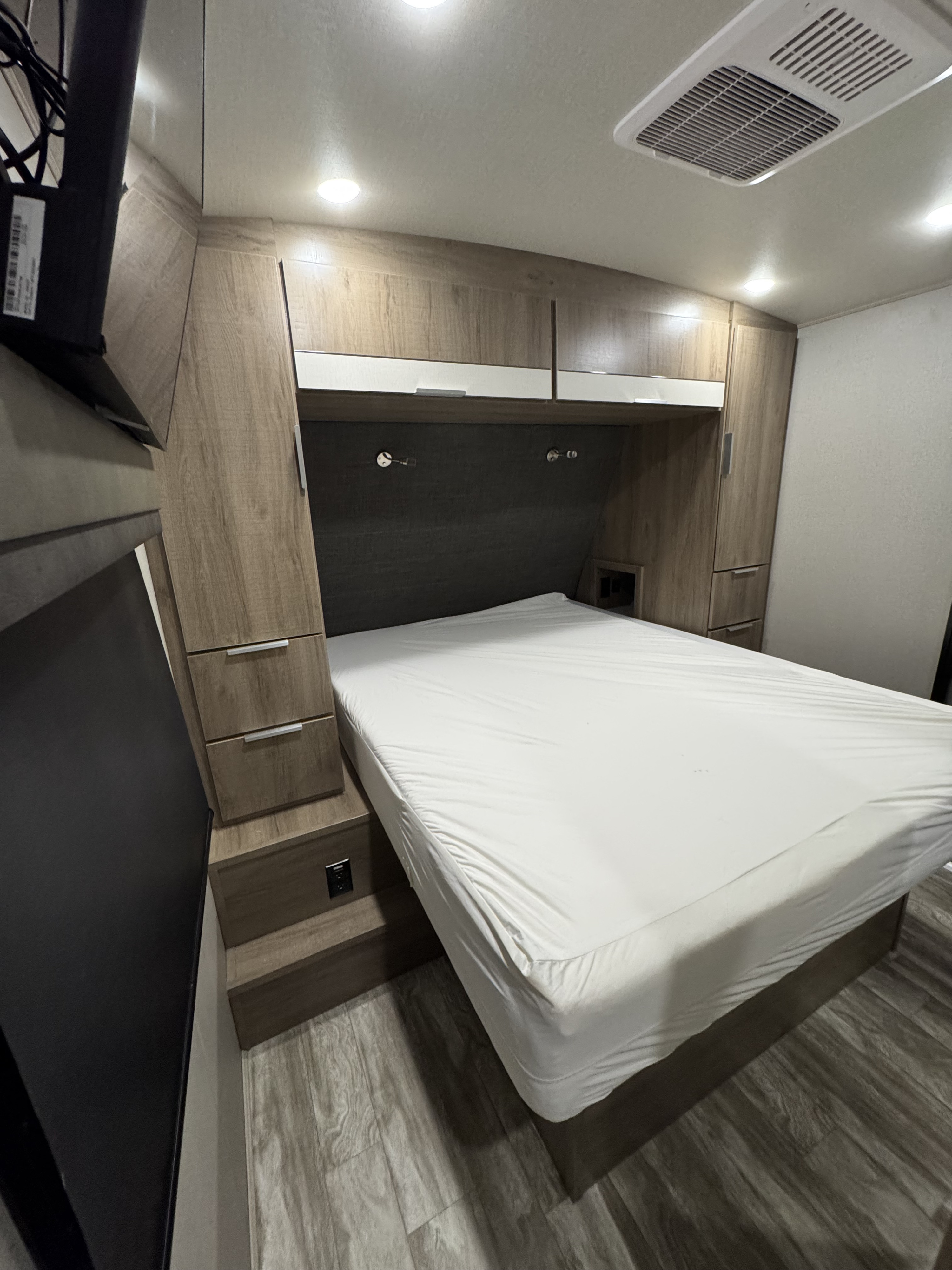 Compact RV rental bedroom featuring a cozy bed, built-in storage, TV, and modern lighting.. Grand Design Imagine 2021