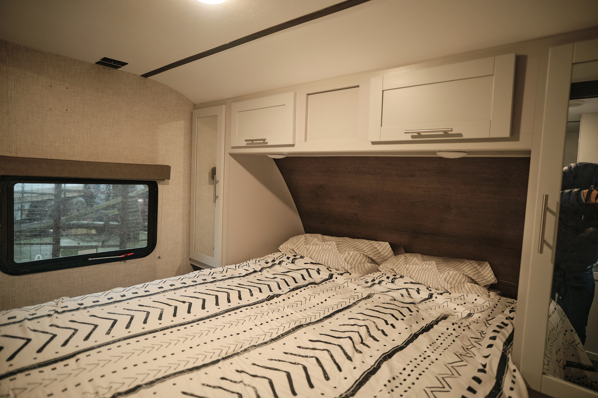 Cozy RV rental bedroom with patterned bed, window view, and overhead storage.. Keystone Bullet 2019