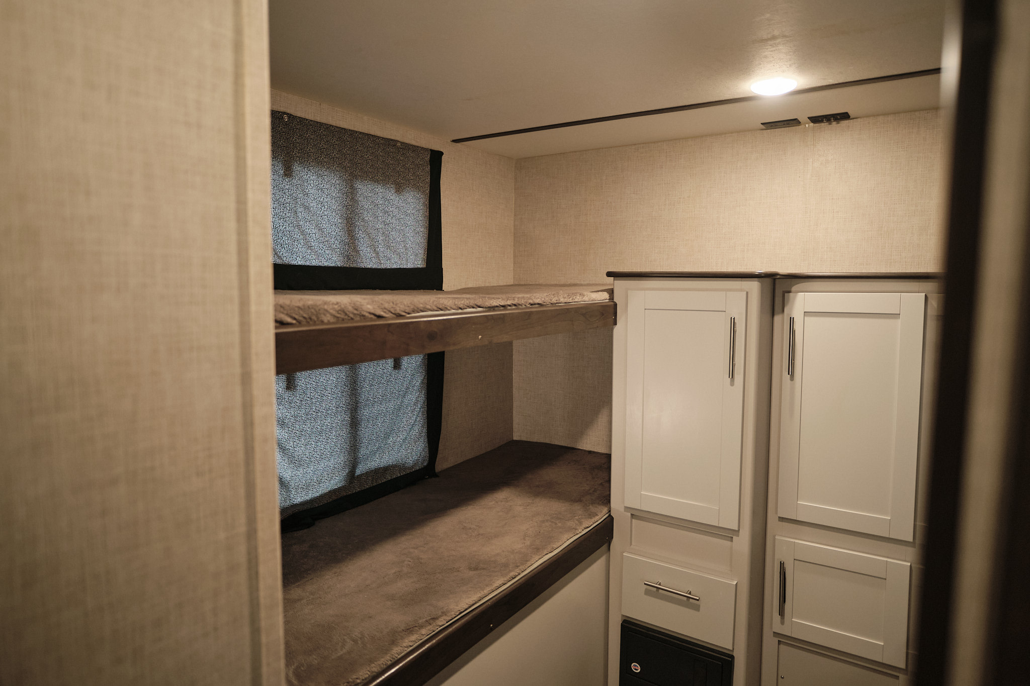 Cozy RV rental interior showing stacked bunk beds with window shades & white storage cabinets.. Keystone Bullet 2019