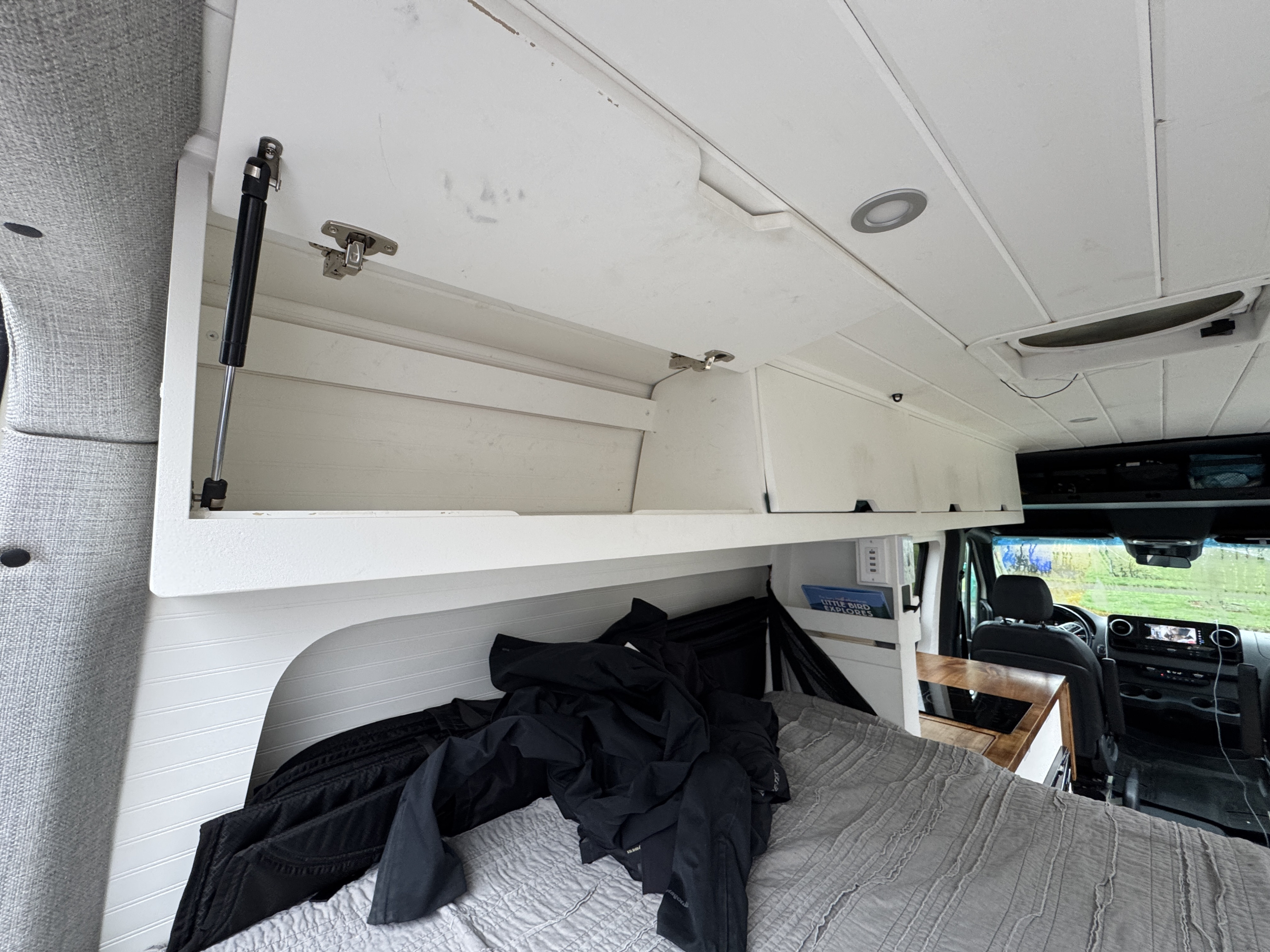 Cozy RV rental interior with bed & overhead storage. Front cab visible, perfect for travel.. Mercedes-Benz Sprinter 2020