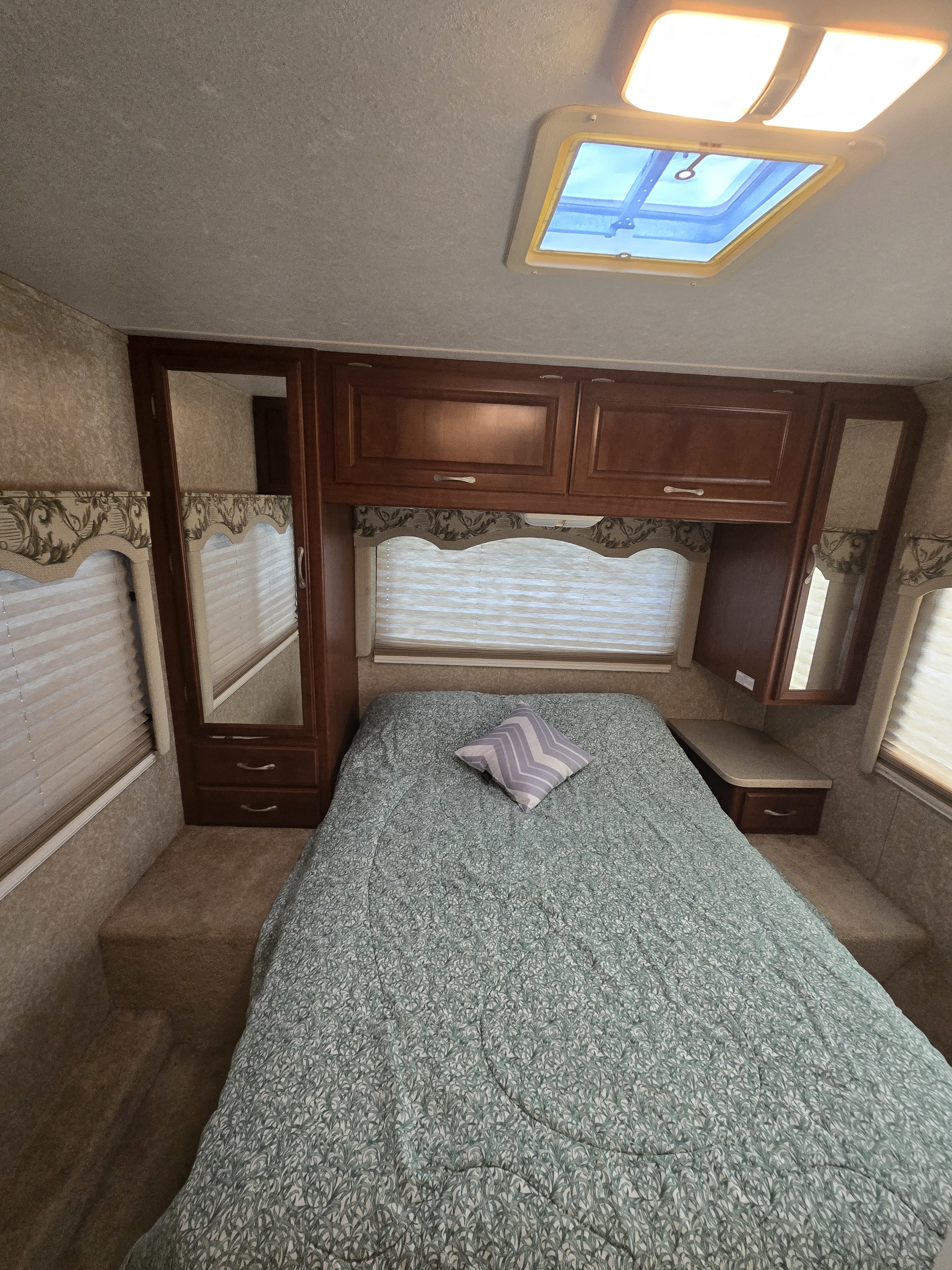 Cozy RV rental bedroom featuring a patterned comforter, mirrored closet, overhead storage, and skylight.. Four Winds Chateau Sport 2006