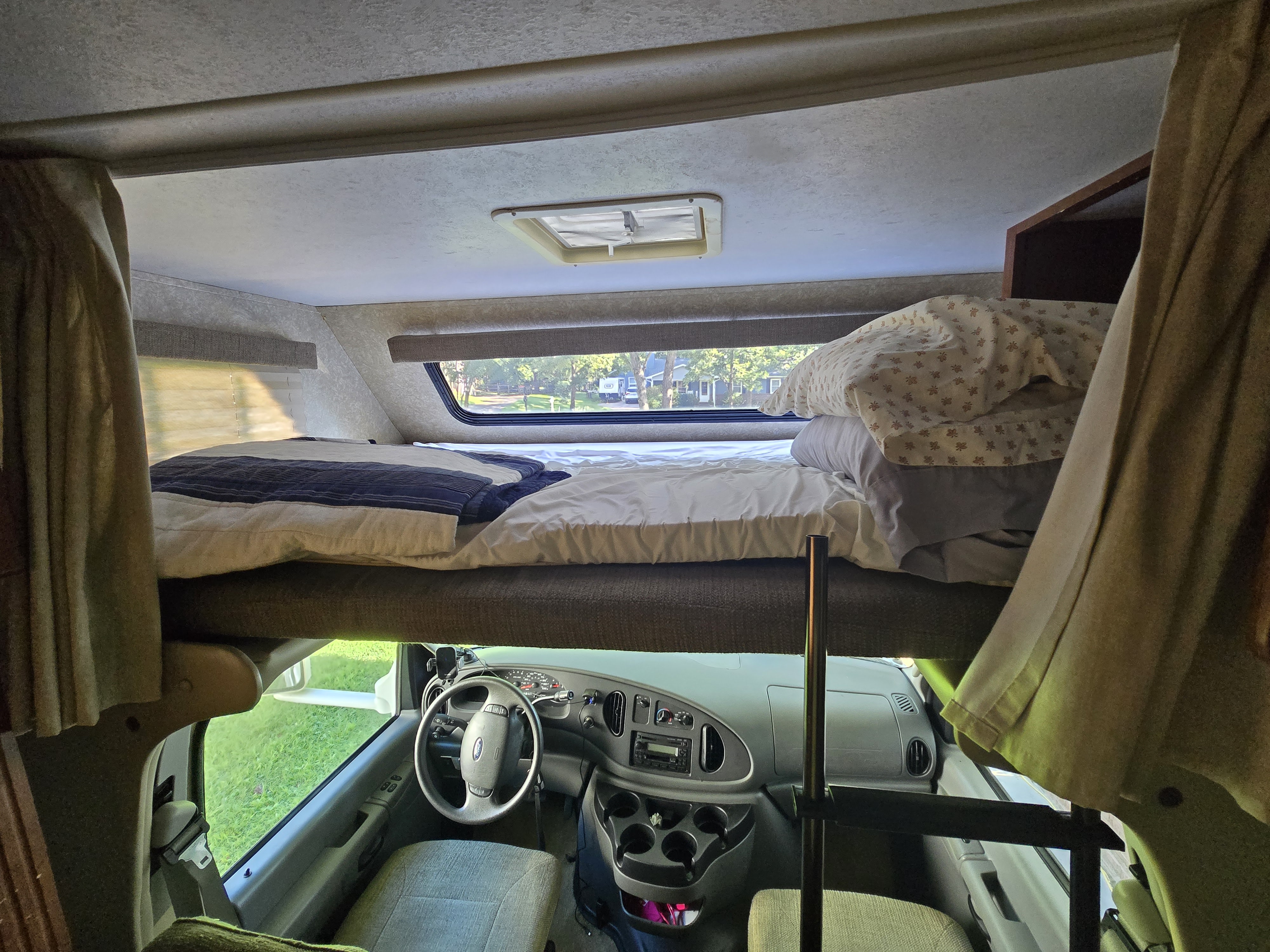 Inside an RV rental: a cozy cab-over bed with a window view above the driver's area and dashboard. Ready for adventure!. Four Winds Chateau Sport 2006