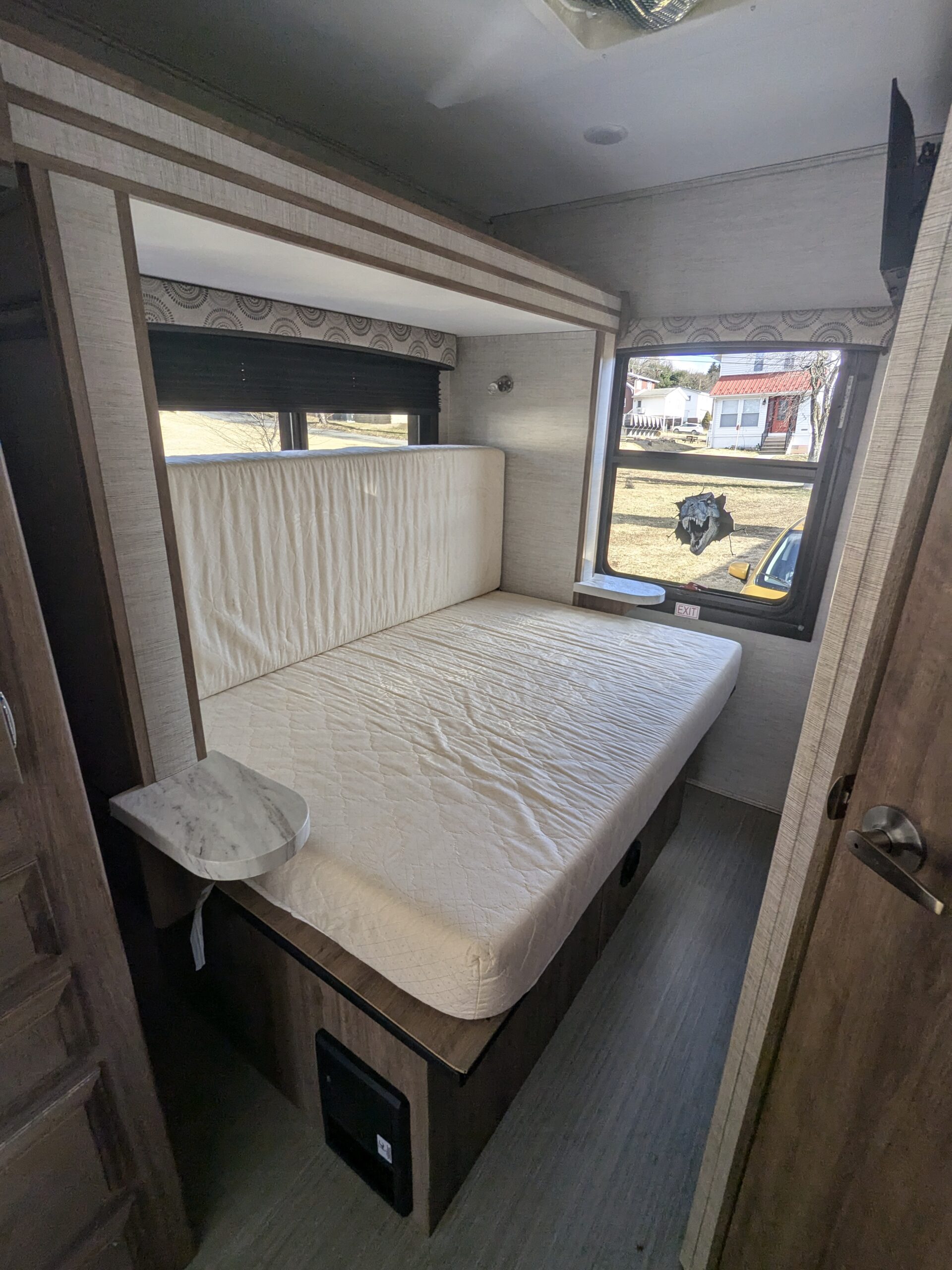 Inside a cozy rv rental, this sleeping area features a comfortable bed, side shelves, and windows with outdoor views.. Entegra Odyssey 2021