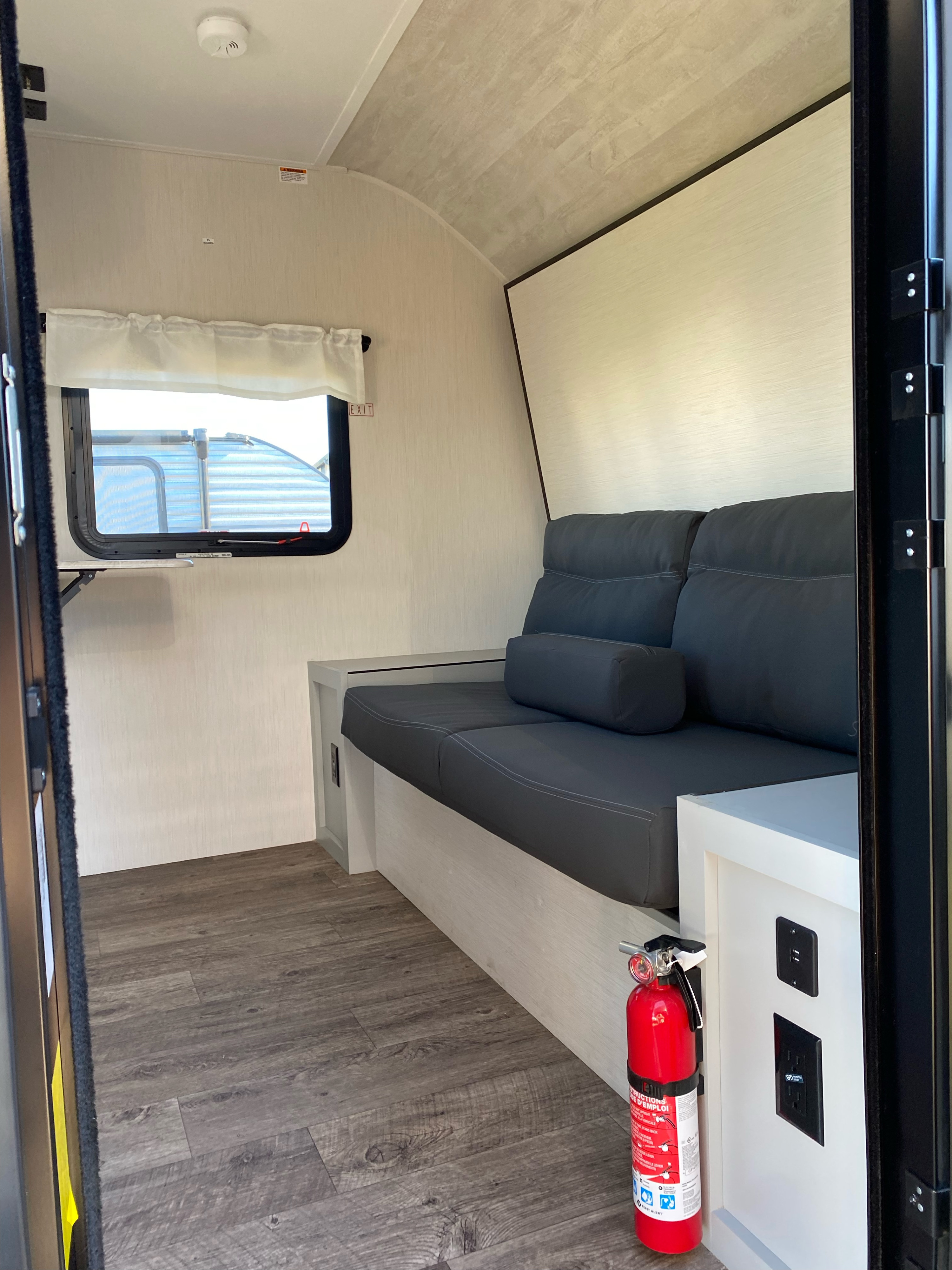 RV rental interior: Cozy sofa, window, wood floor, and safety features like a fire extinguisher and power outlets.. Forest River Vibe 2022