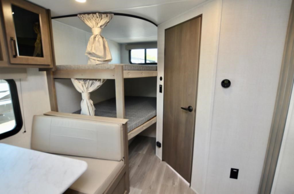 RV rental interior: Cozy bunk beds with privacy curtains, a comfortable dinette, and a door leading to private space.. Grand Design Transcend XPLOR 26BHX 2025