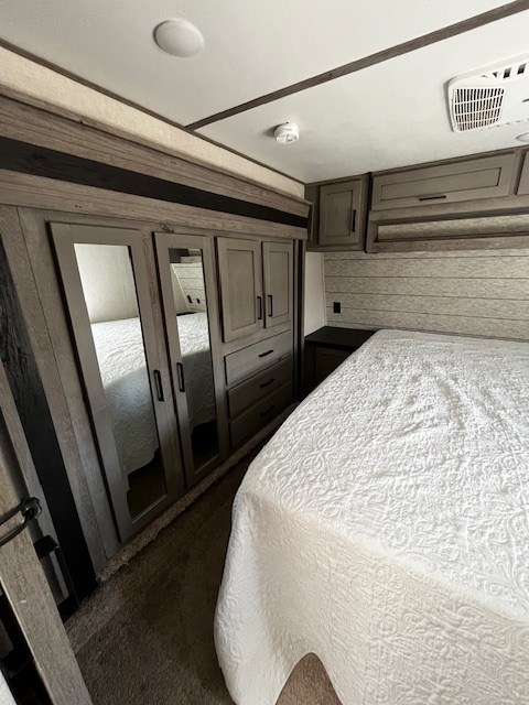 Inside an RV rental: a modern bedroom featuring a bed with white quilt, mirrored closet, and wood-paneled walls.. Keystone Raptor 2020