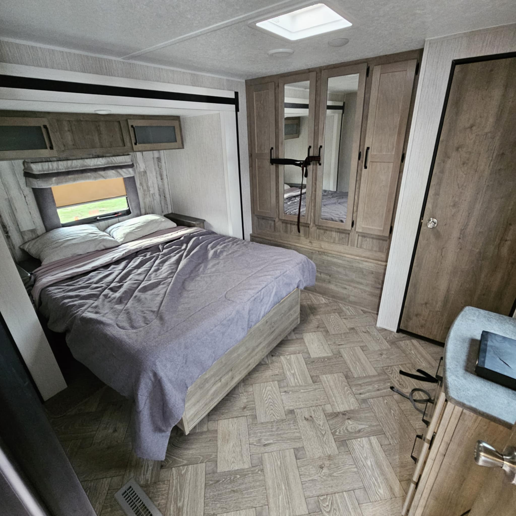 Cozy RV rental bedroom featuring a comfy bed, mirrored wardrobe, overhead cabinets, and patterned flooring. Ready for travel!. Forest River Palomino Puma 2021