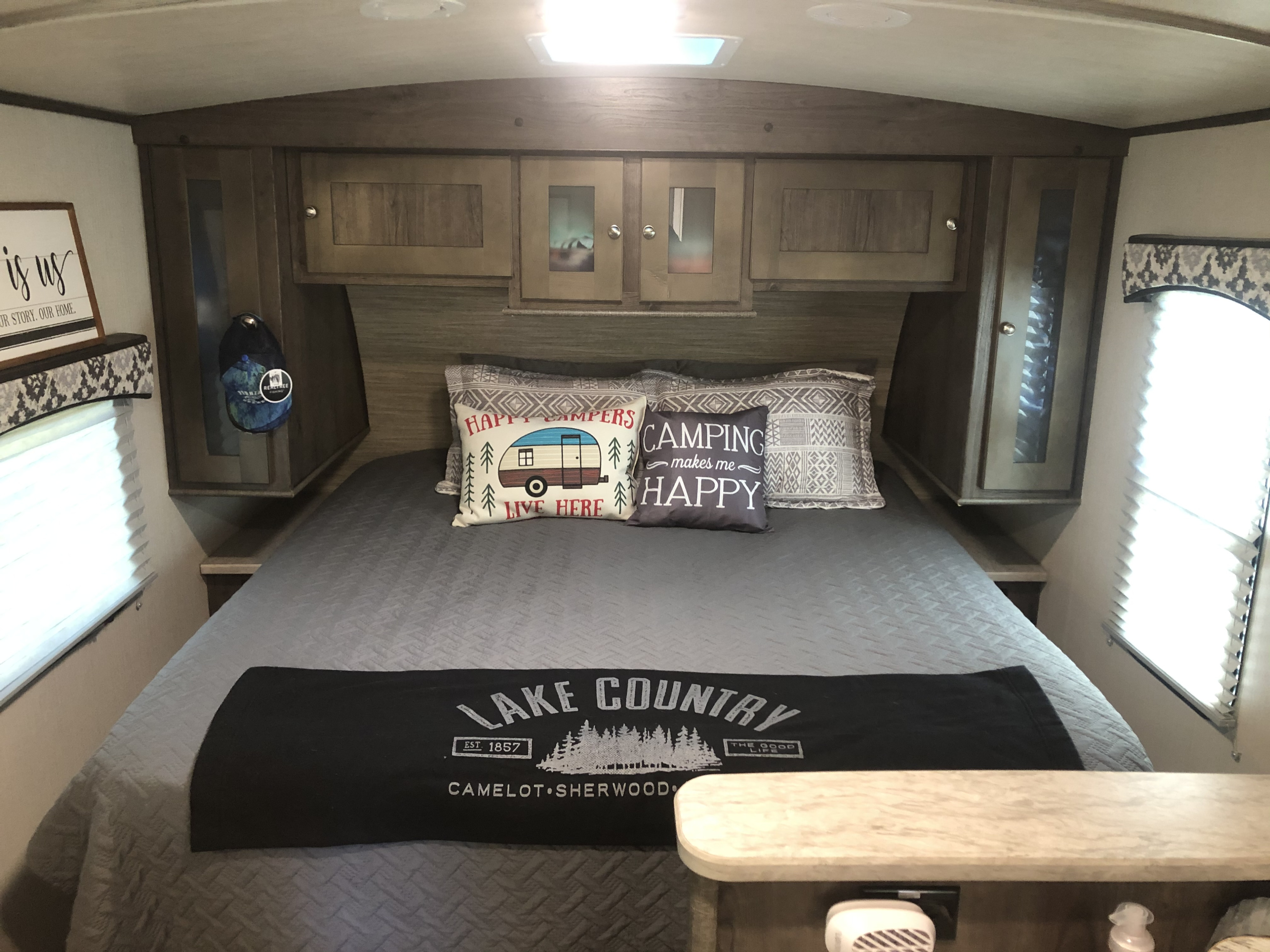 Cozy RV rental bedroom featuring a quilted bed, camping-themed pillows, and convenient overhead cabinets for storage.. Cruiser RV MPG Ultra Lite 2018
