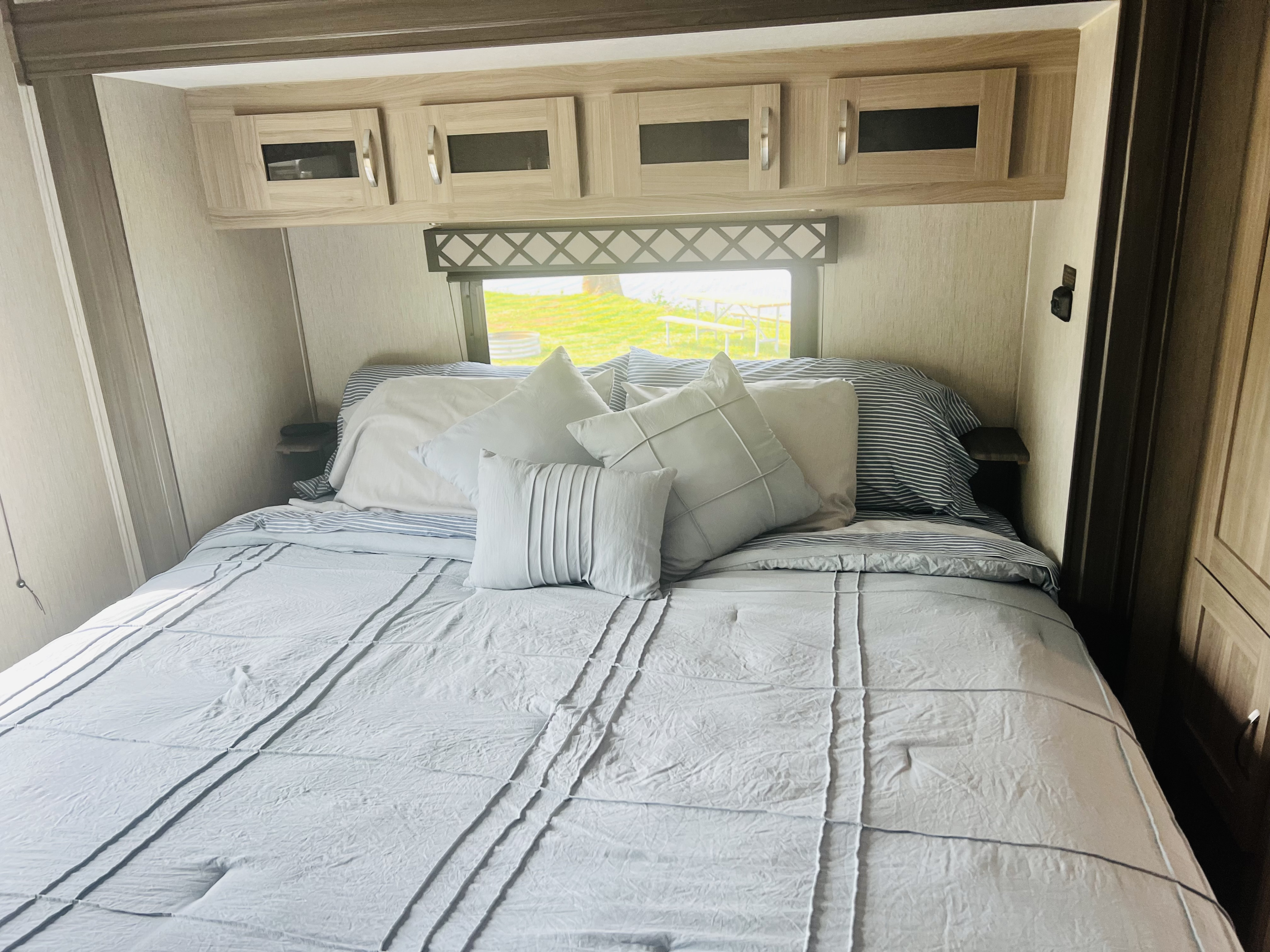 Inside an RV rental: a bright, comfy bedroom with sleek cabinets & a scenic window view.. Coachmen Freedom Express 2020