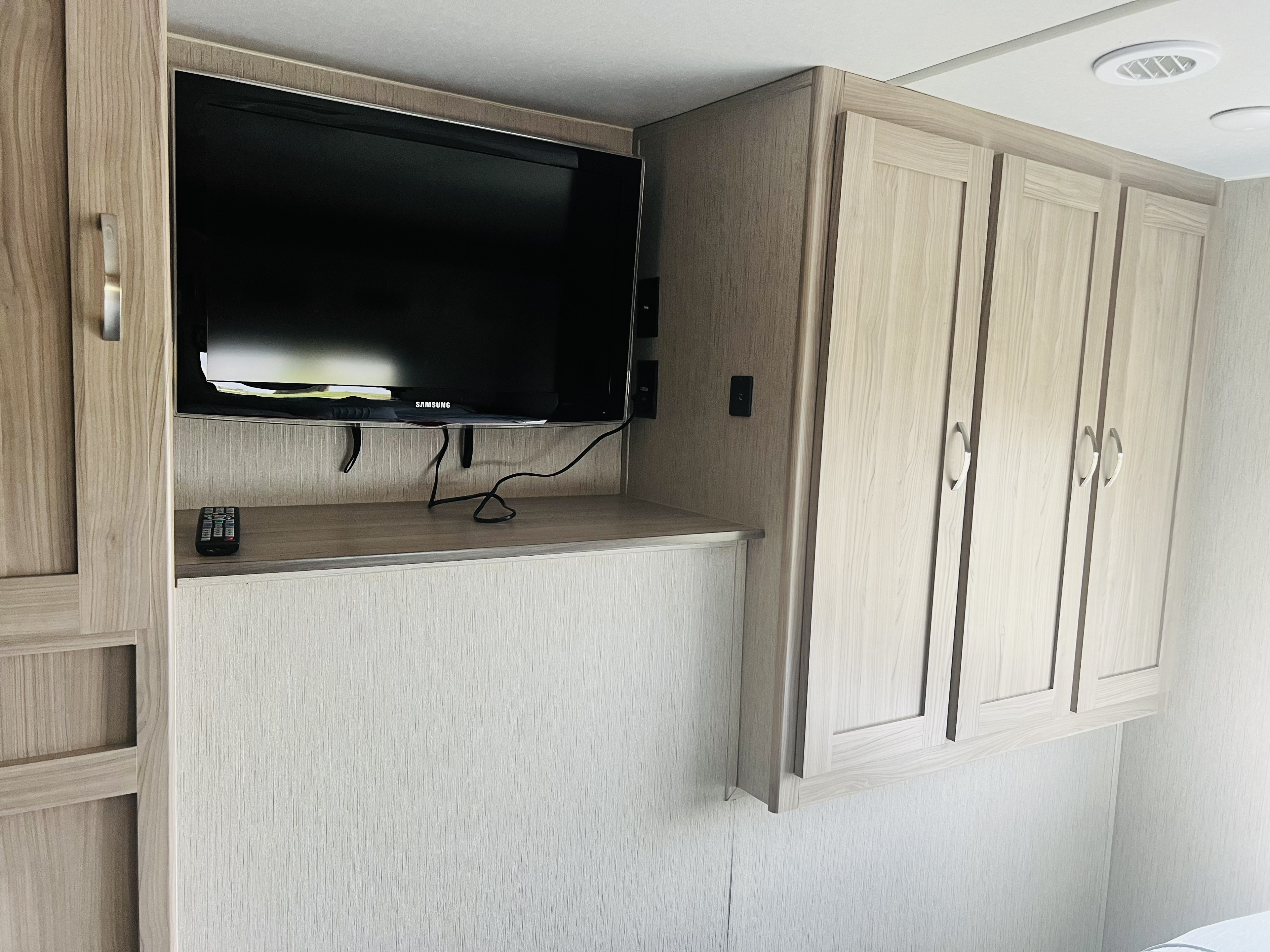RV rental interior: A flat-screen TV sits on a shelf, flanked by light-toned storage cabinets.. Coachmen Freedom Express 2020
