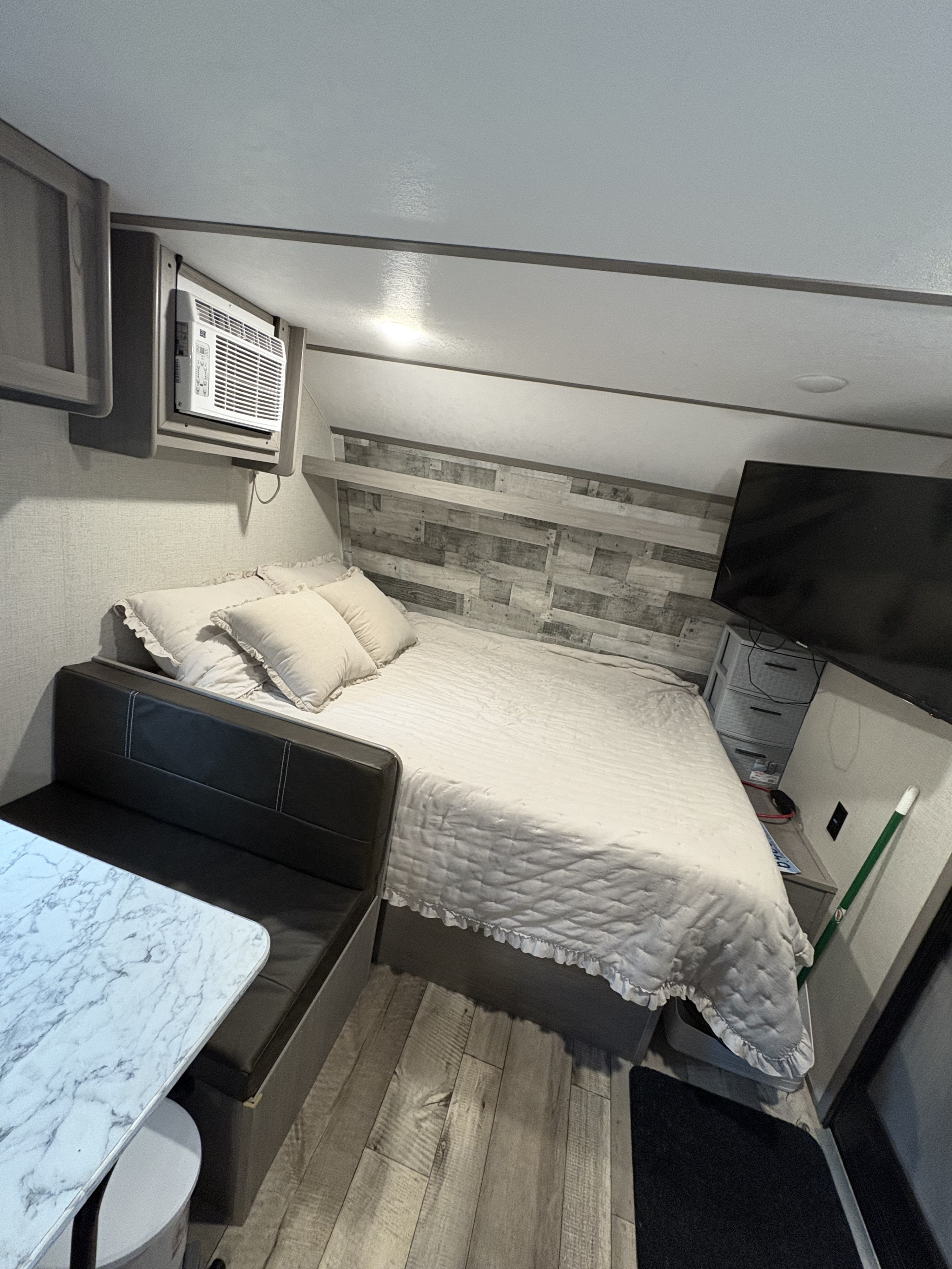 Cozy RV rental interior: a comfy bedroom with rustic accent wall, AC, and adjacent compact dining area.. Keystone RV Coleman 2023