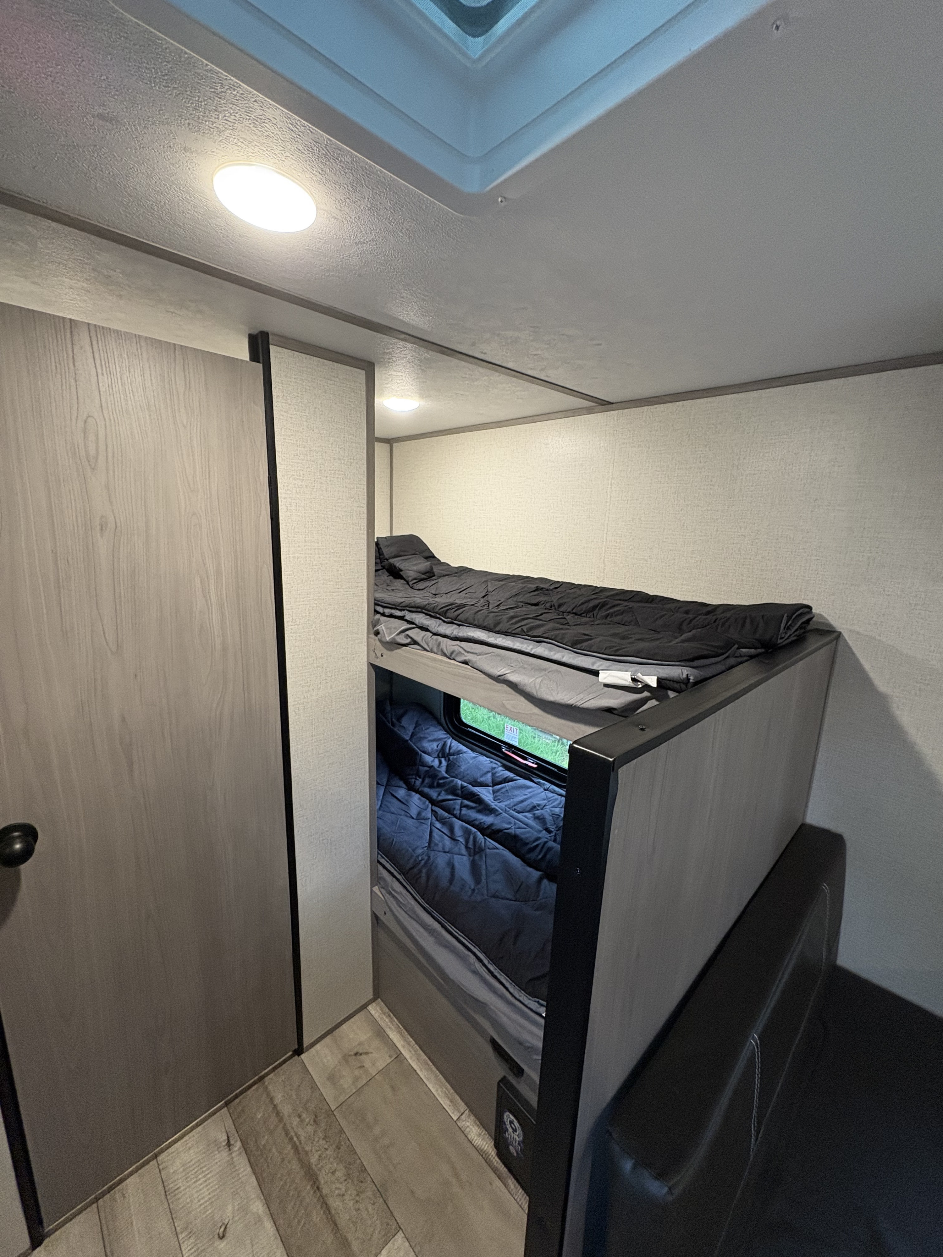 Inside an RV rental: two bunk beds with bedding, a door, and a cozy seating area for compact living.. Keystone RV Coleman 2023