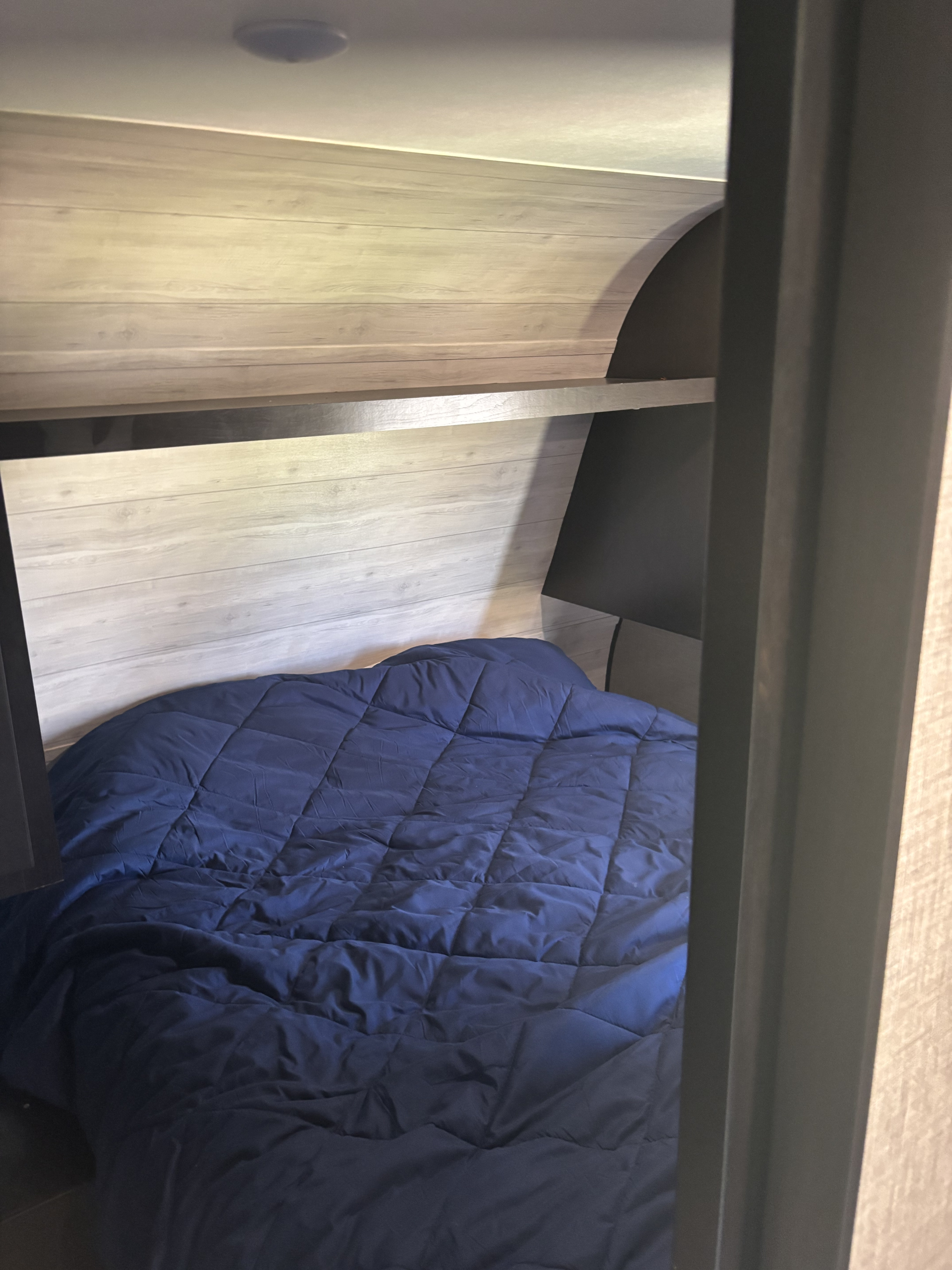Cozy RV rental bunk with blue comforter, wood walls, and storage shelf. Ideal for a compact sleeping area.. Jayco Jay Flight SLX 2022