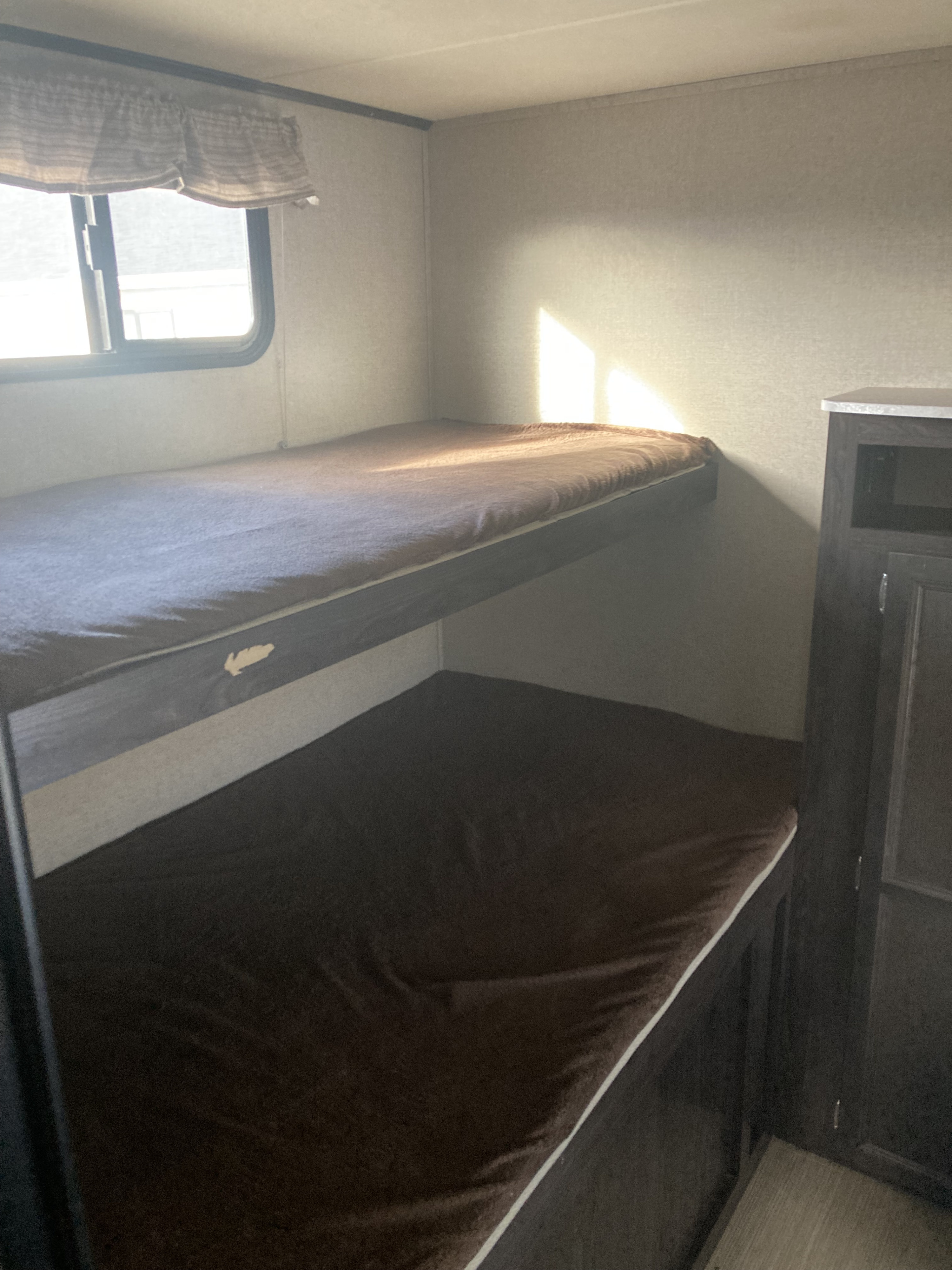Inside an RV rental: cozy bunk beds with soft brown blankets, a window, and a cabinet provide comfortable sleeping.. Dutchmen Kodiak Ultra Lite 2019