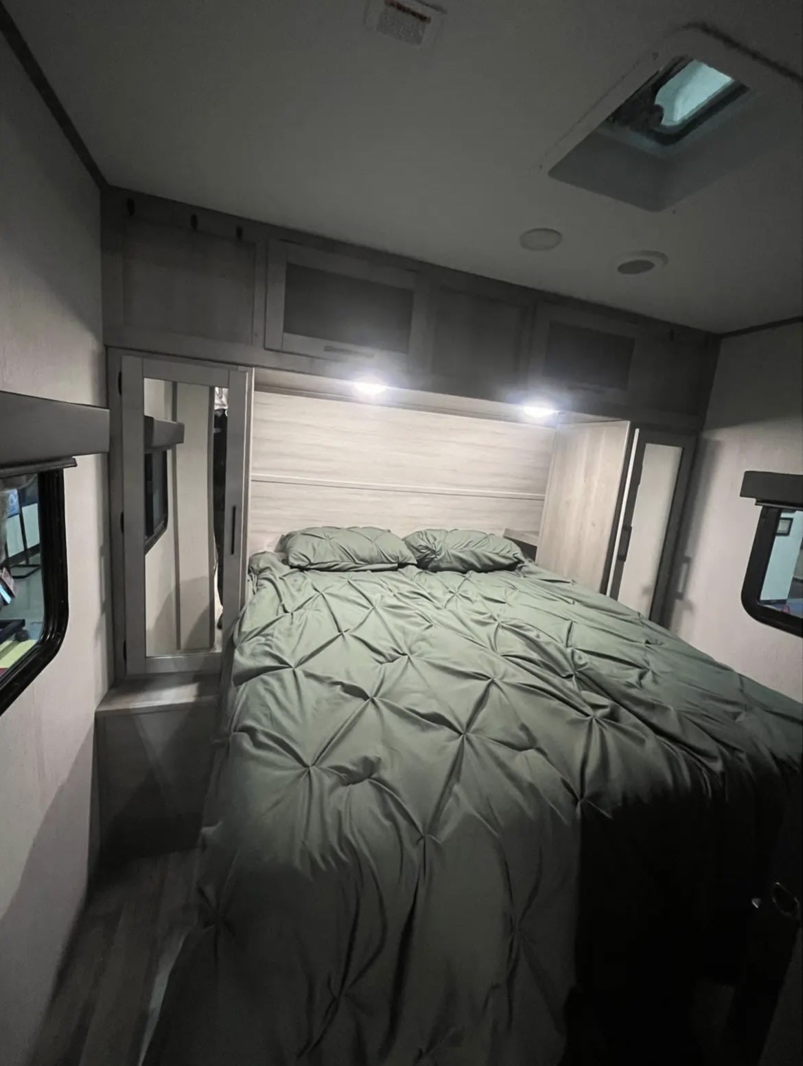 RV rental's cozy bedroom: green comforter, overhead storage, and ample light from windows & ceiling fixtures.. Dutchmen Kodiak Ultra Lite 2019