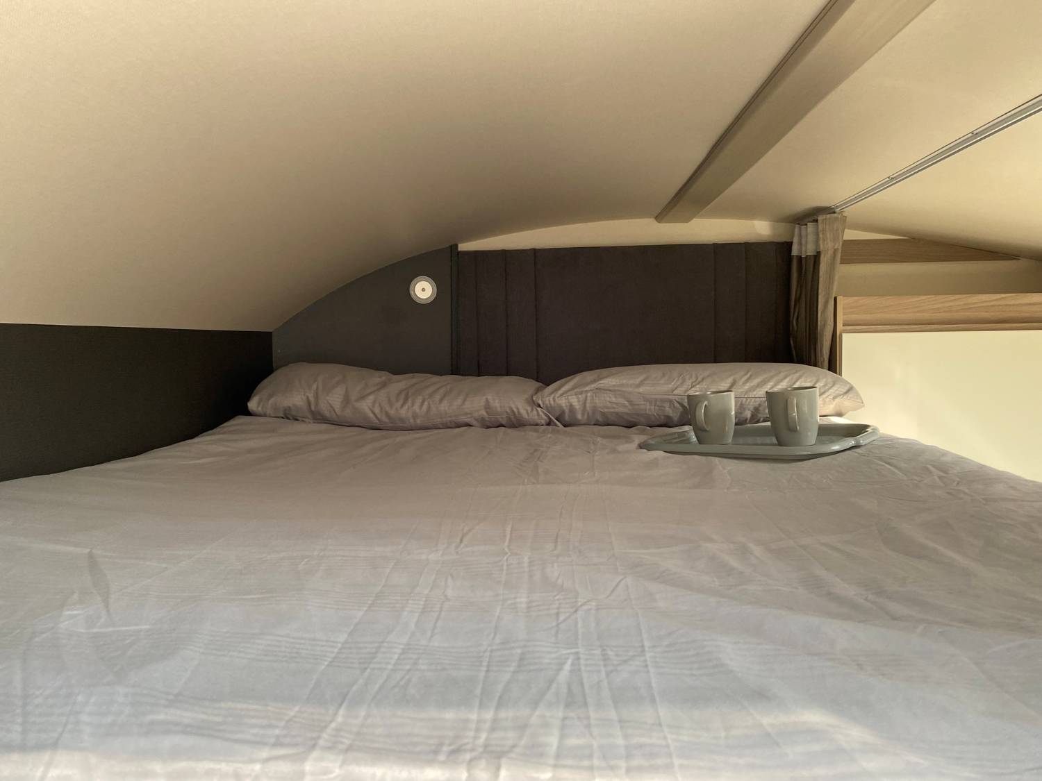 Cozy RV rental bedroom featuring a made bed with pillows, a tray holding two mugs, and an arched ceiling.. Swift Voyager 485 2024