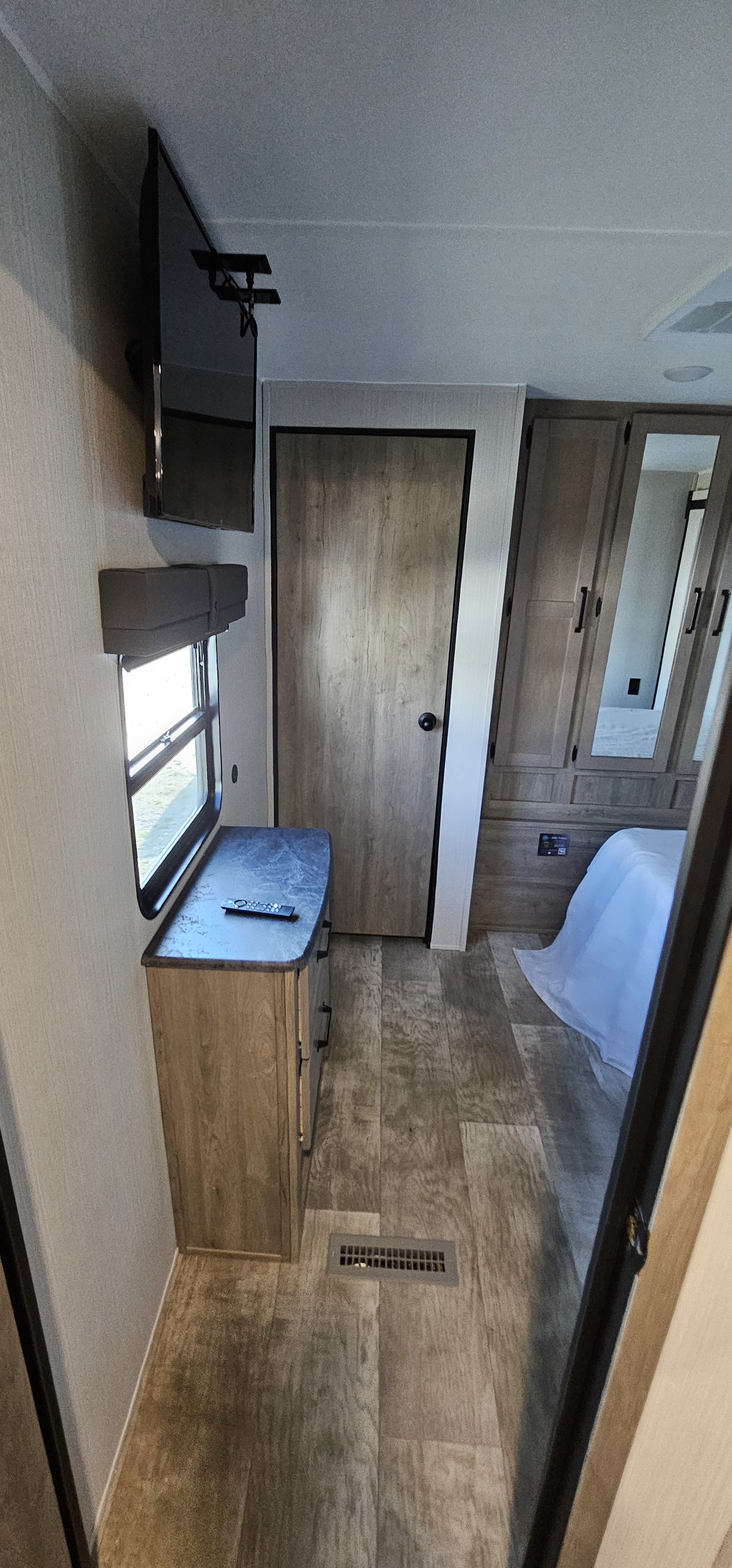RV rental bedroom interior: Features a mounted TV, window with blind, dresser, door, and built-in wardrobe with bed.. Forest River Puma 2025