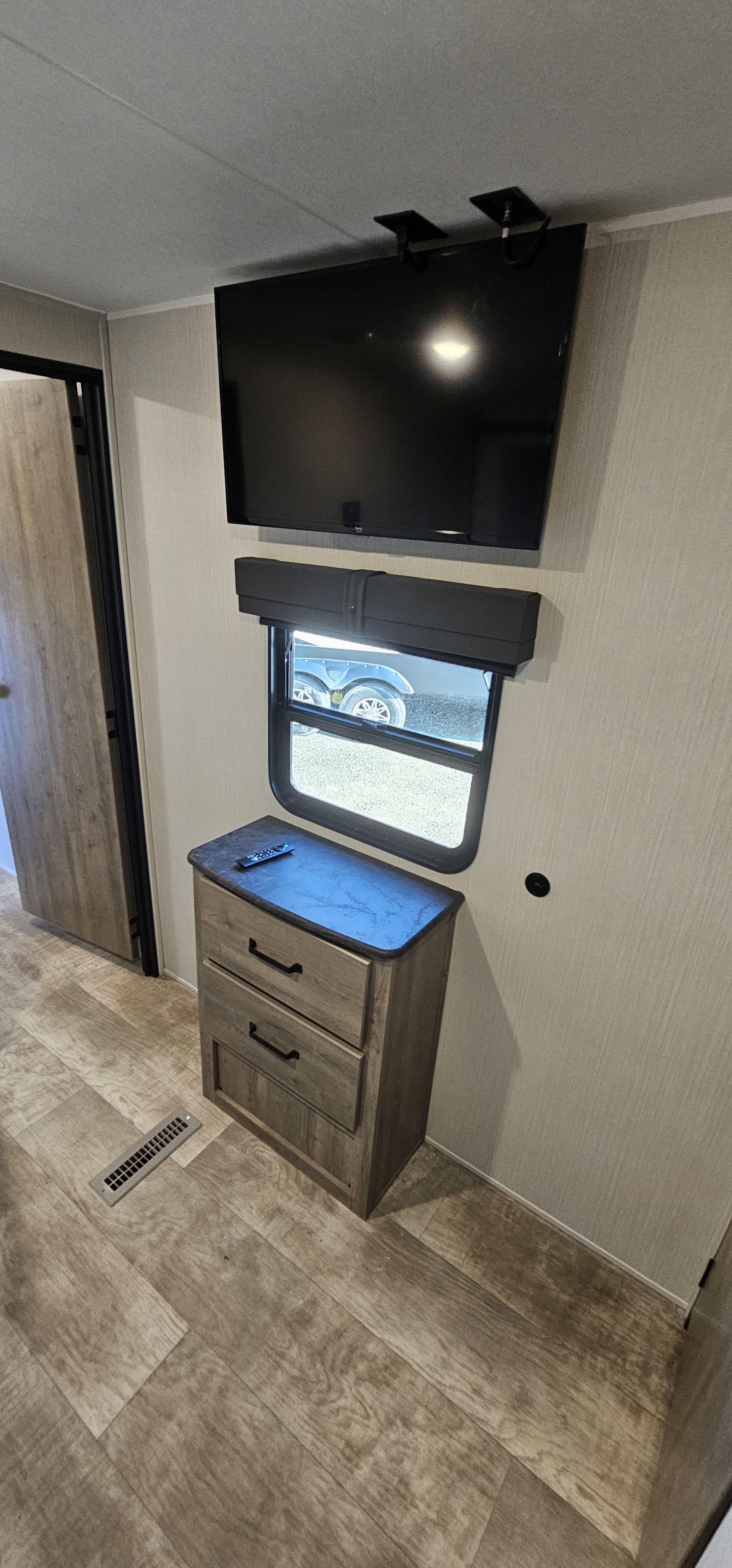 RV rental bedroom with a wall-mounted TV, window with shade, a two-drawer dresser, and wood-look flooring.. Forest River Puma 2025