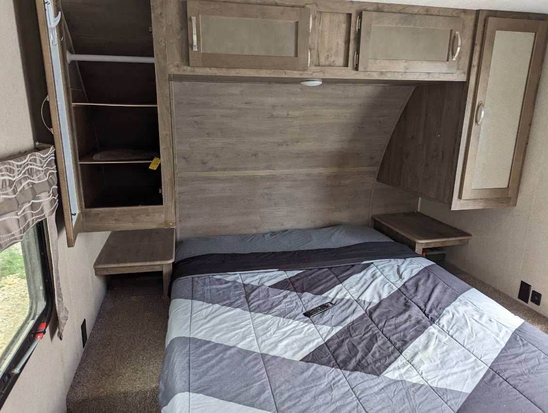 RV rental bedroom with patterned bedspread, ample overhead cabinets, and side storage. A compact, functional space.. Forest River Palomino Puma 2020