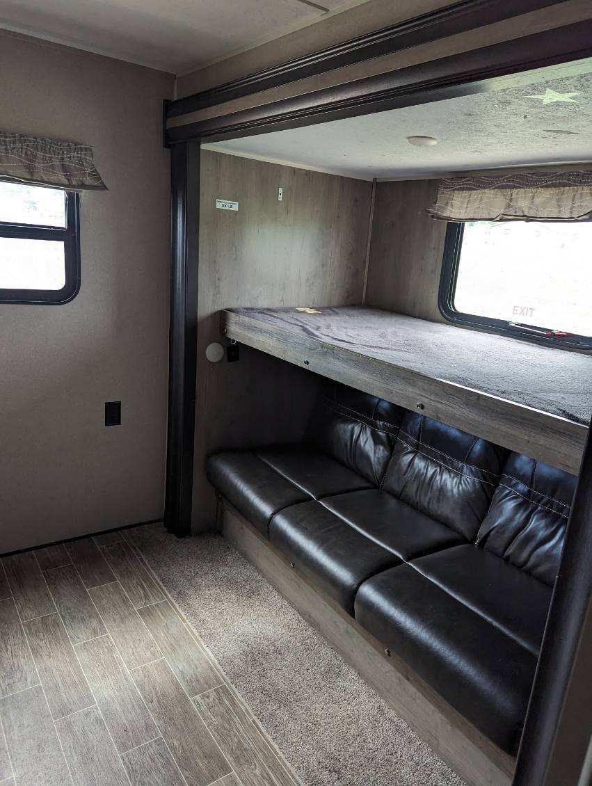 This cozy RV rental interior features a bunk bed above a black leather sofa, with mixed flooring and a window.. Forest River Palomino Puma 2020