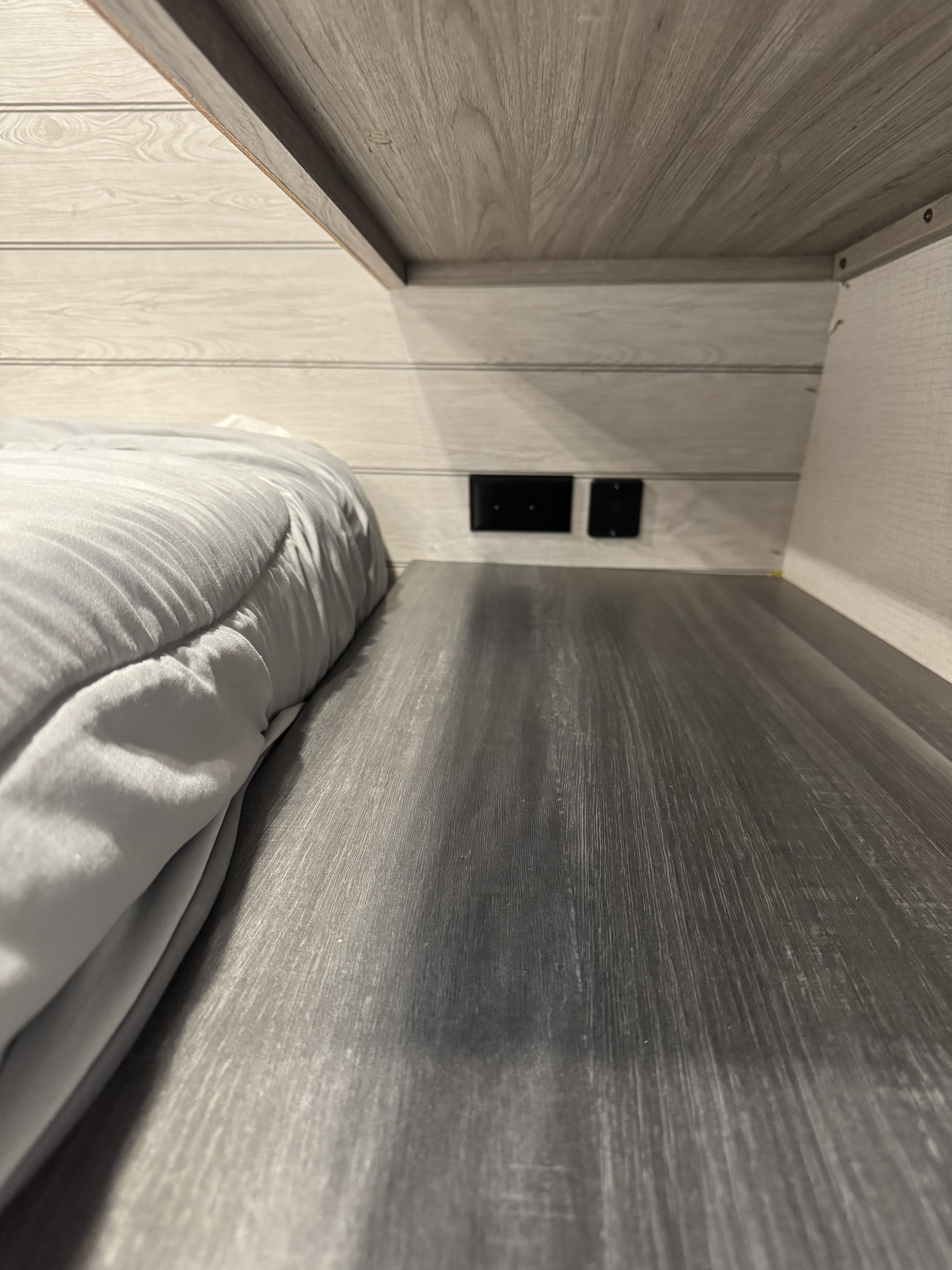 Inside a cozy RV rental bunk, featuring light gray wood-grain walls, dark gray sleeping platform, and charging outlets.. Keystone RV Passport SL 2022