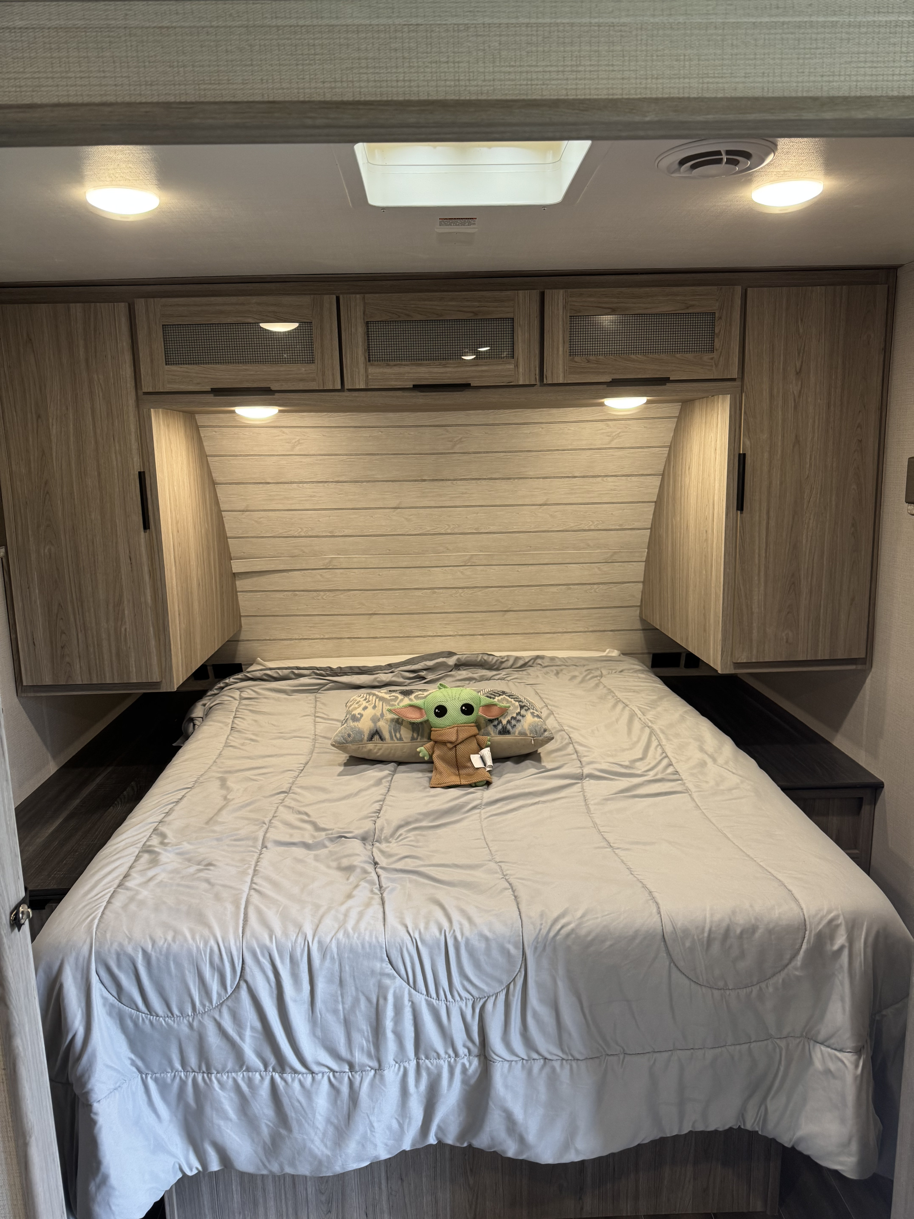 Modern RV rental bedroom featuring a cozy bed, overhead cabinets, Grogu, and a skylight for natural light.. Keystone RV Passport SL 2022