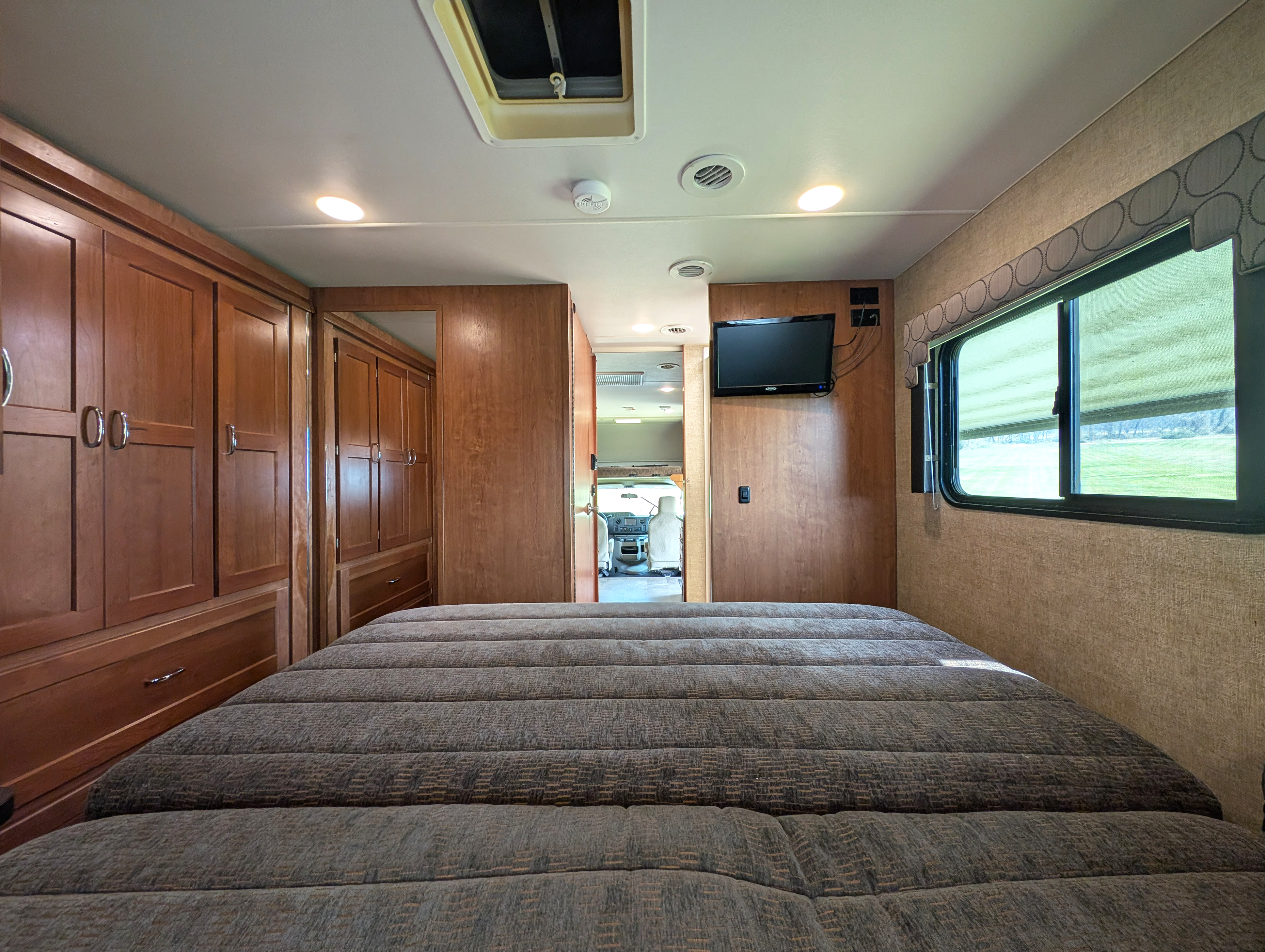 This RV rental offers a comfortable bedroom with a large bed, ample wood cabinets, TV, and window views.. Winnebago Spirit 2018