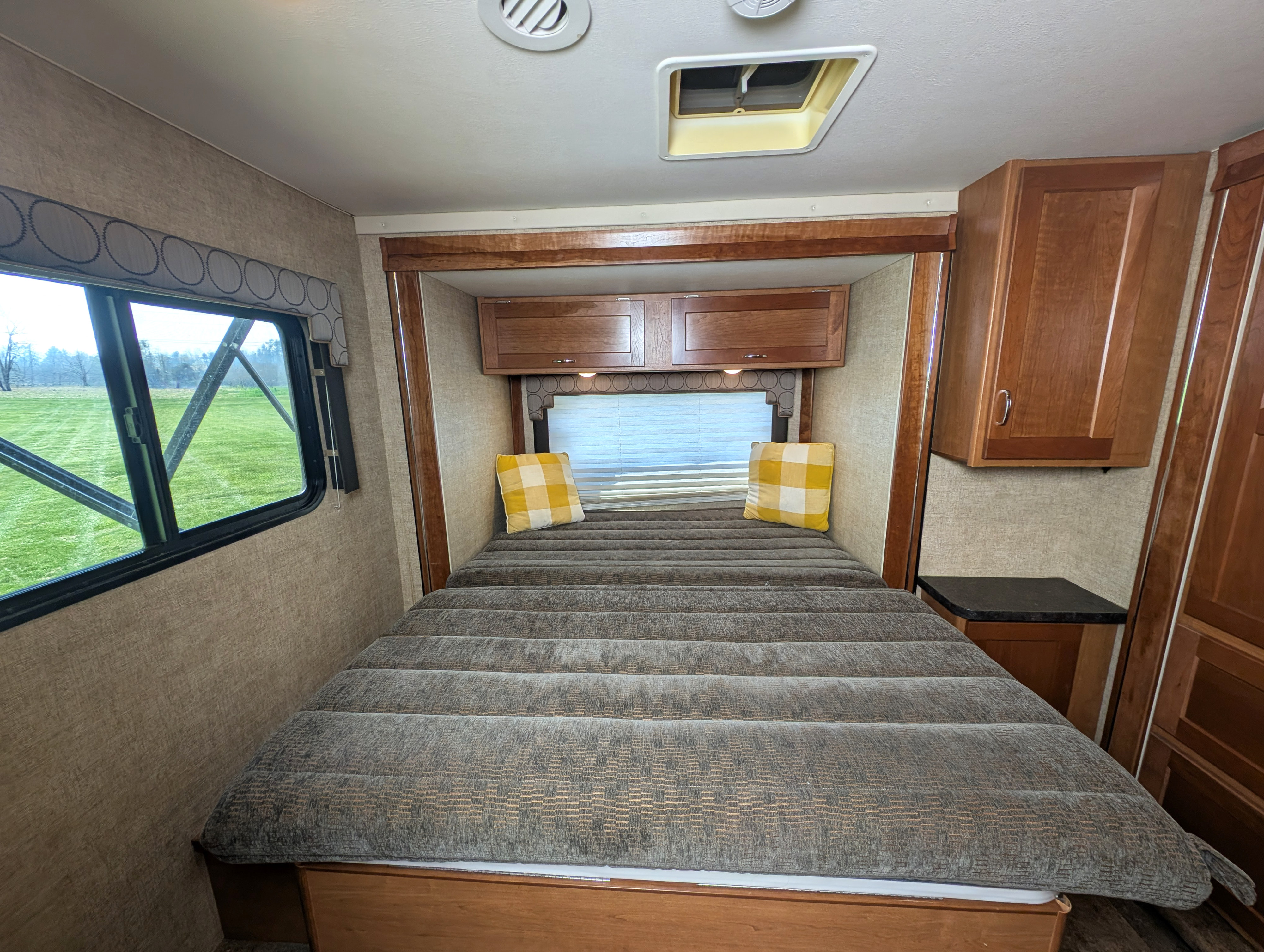 Inside an RV rental: a comfortable bedroom with a textured bed, window, wooden cabinets, and skylight.. Winnebago Spirit 2018