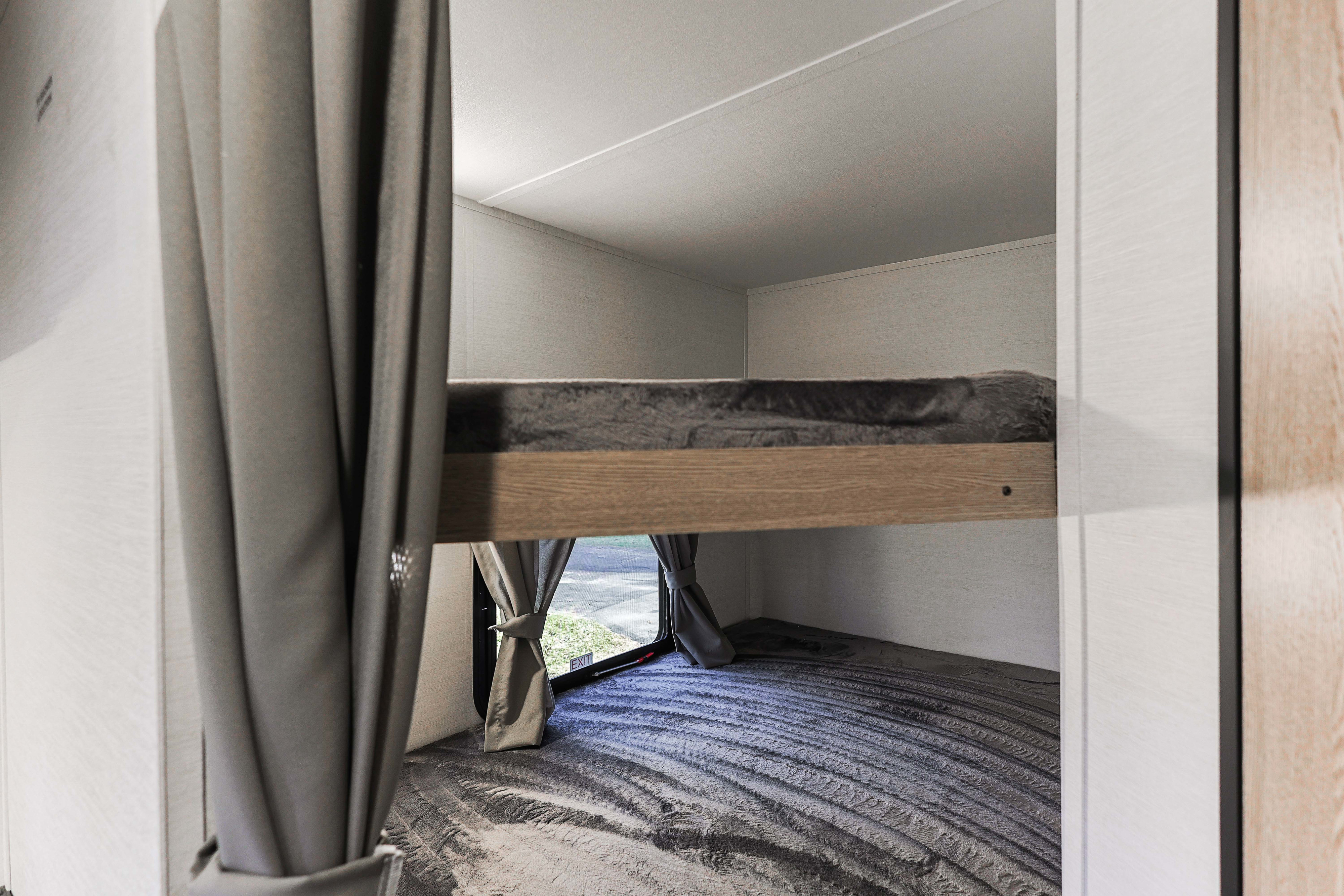 Modern RV rental bunk beds with grey bedding and an emergency exit window, perfect for family travel.. Grand River 36DB 2025