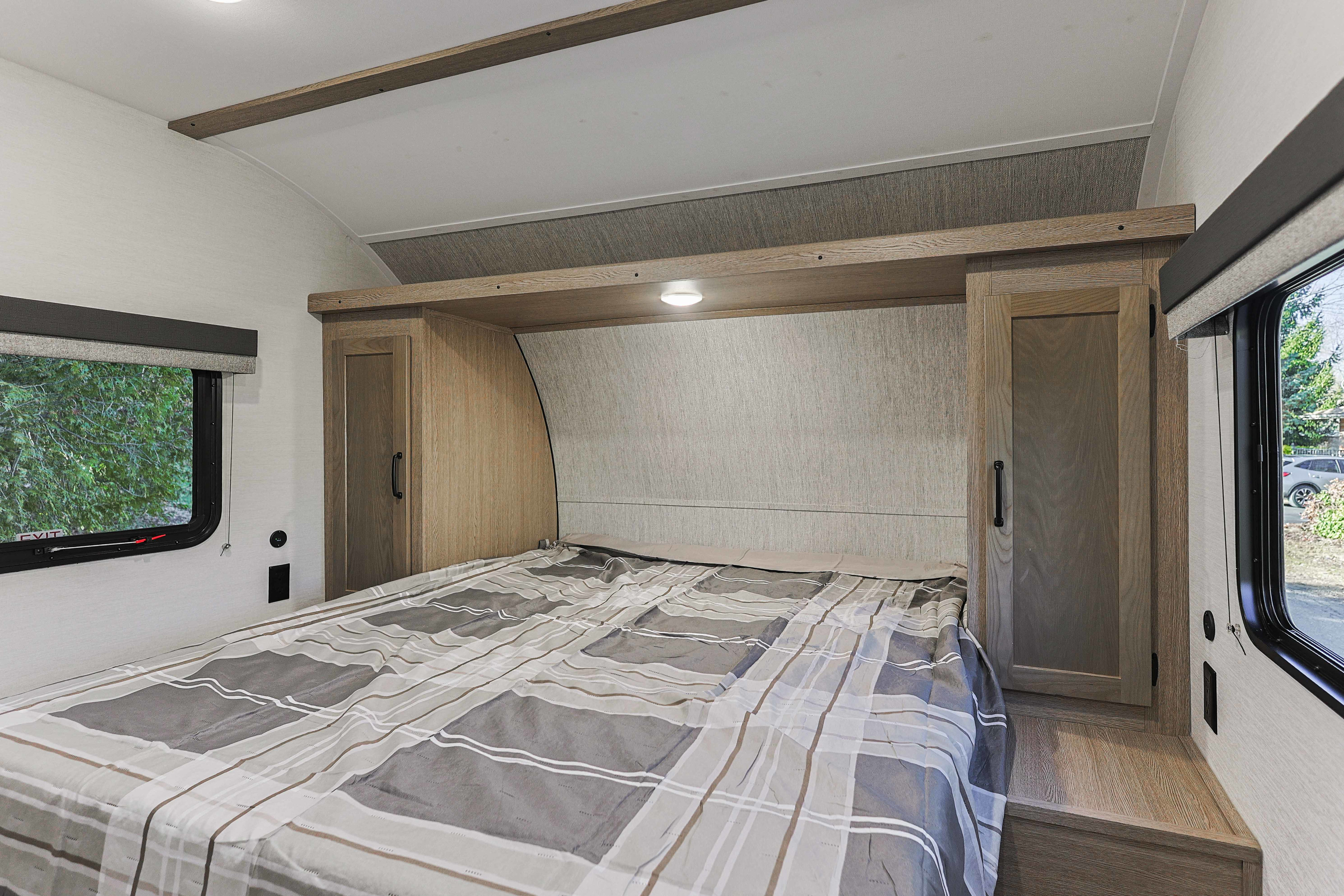 Inside an RV rental: a bedroom with a plaid-covered bed, built-in side cabinets, overhead storage, and windows on each side.. Grand River 36DB 2025
