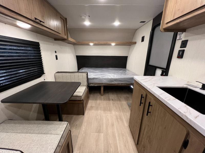 RV rental interior showing a dinette with table & benches, a kitchen with sink, and a bed at the rear wall.. Forest River Cherokee Wolf Pup 16LP 2025