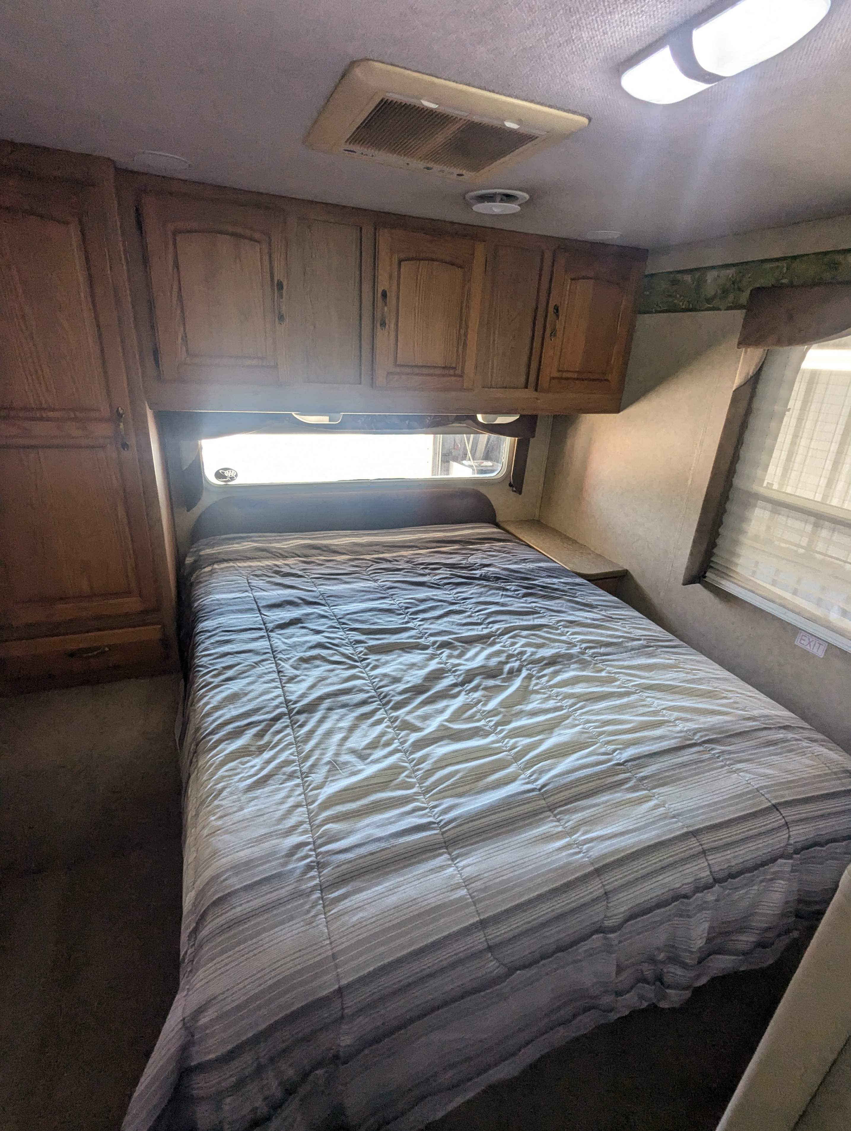 RV rental bedroom with a cozy striped bed, ample overhead wooden cabinets, and a bright window.. Jayco Greyhawk 2006