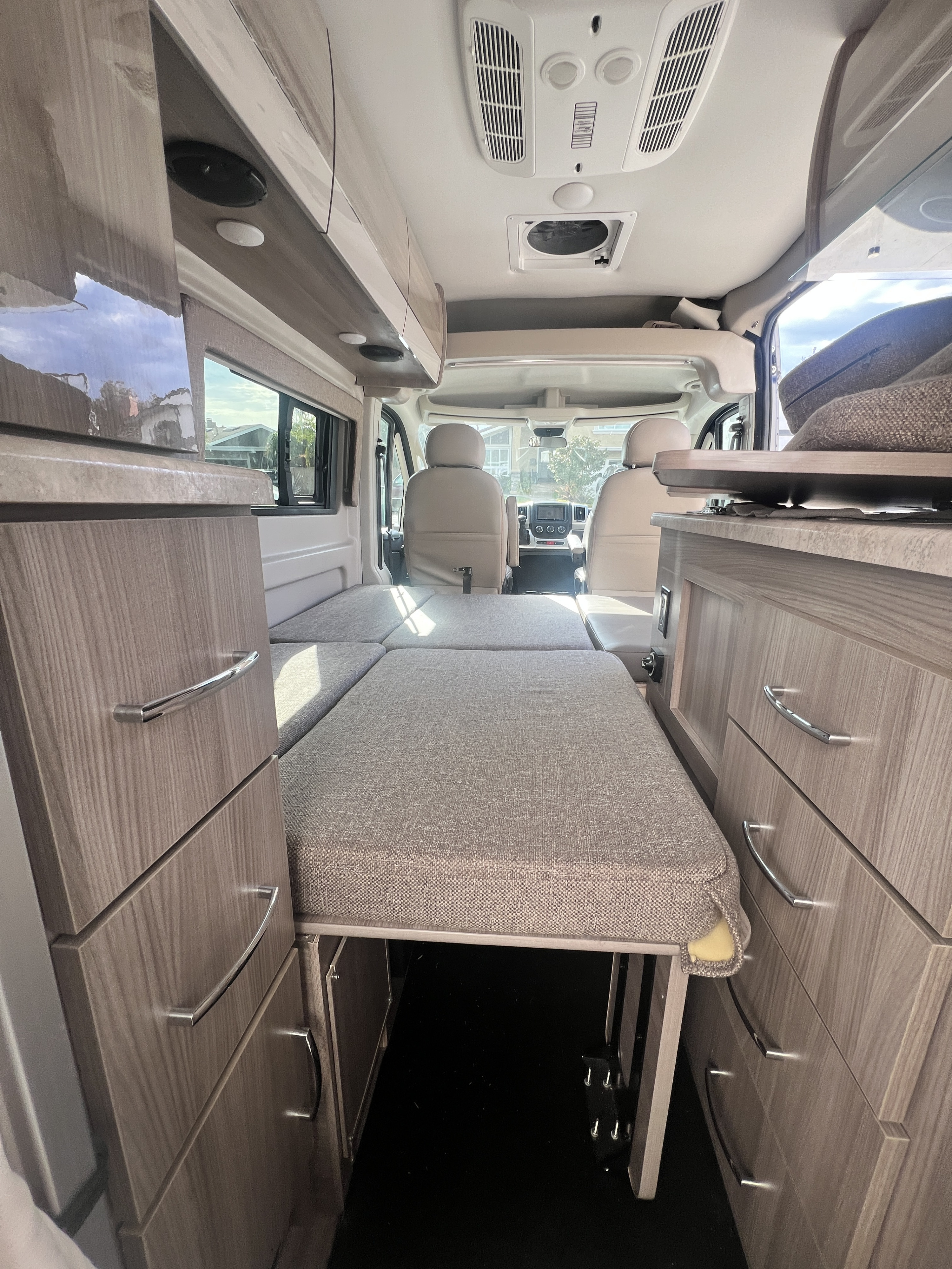 RV rental interior: Cozy camper van with convertible bed, wood-grain cabinets, and a view to the front cab.. Thor Scope 2022