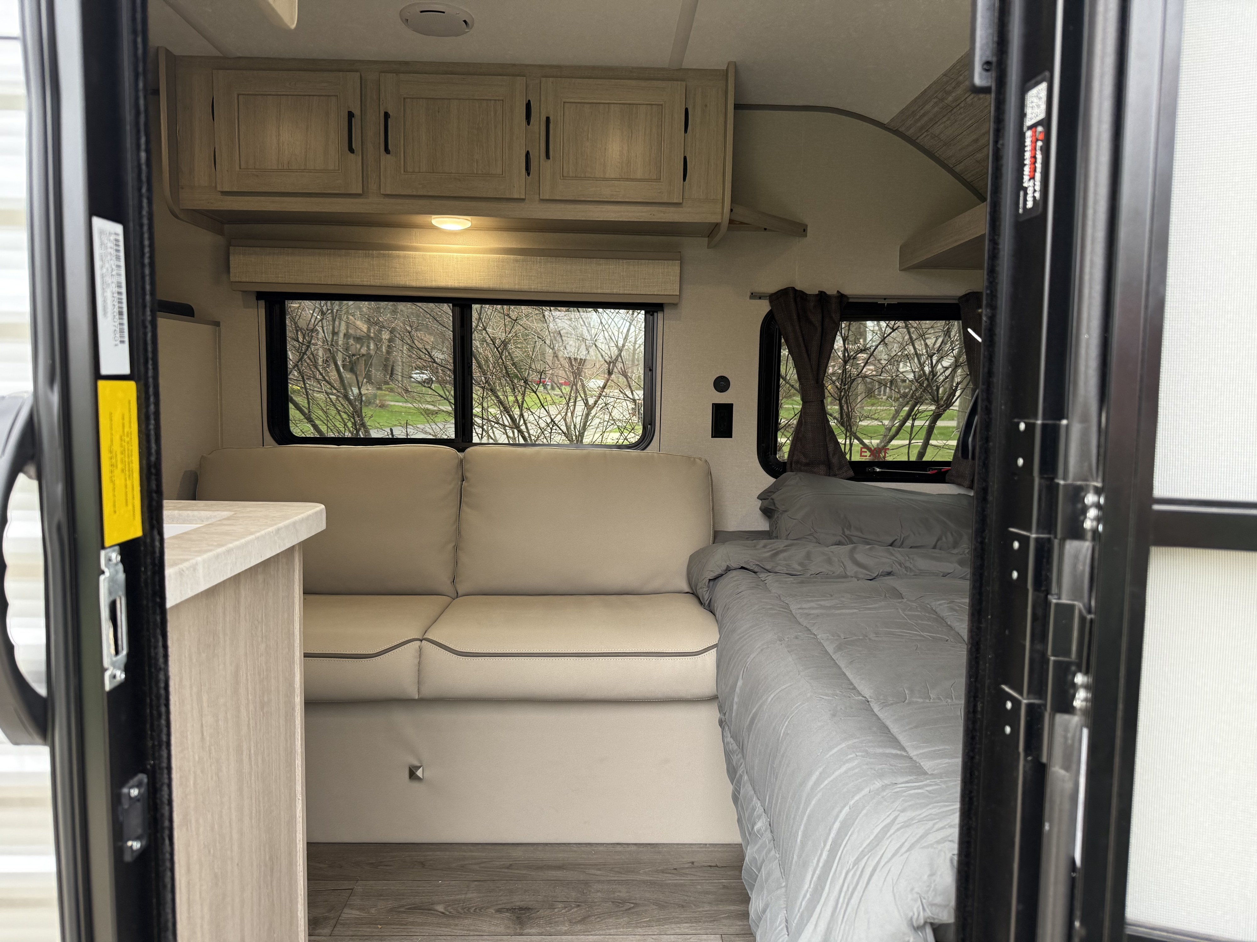 A cozy RV rental interior shows a light-colored sofa, a bed with gray bedding, and a small counter.. Forest River Coachmen Catalina Summit 2024