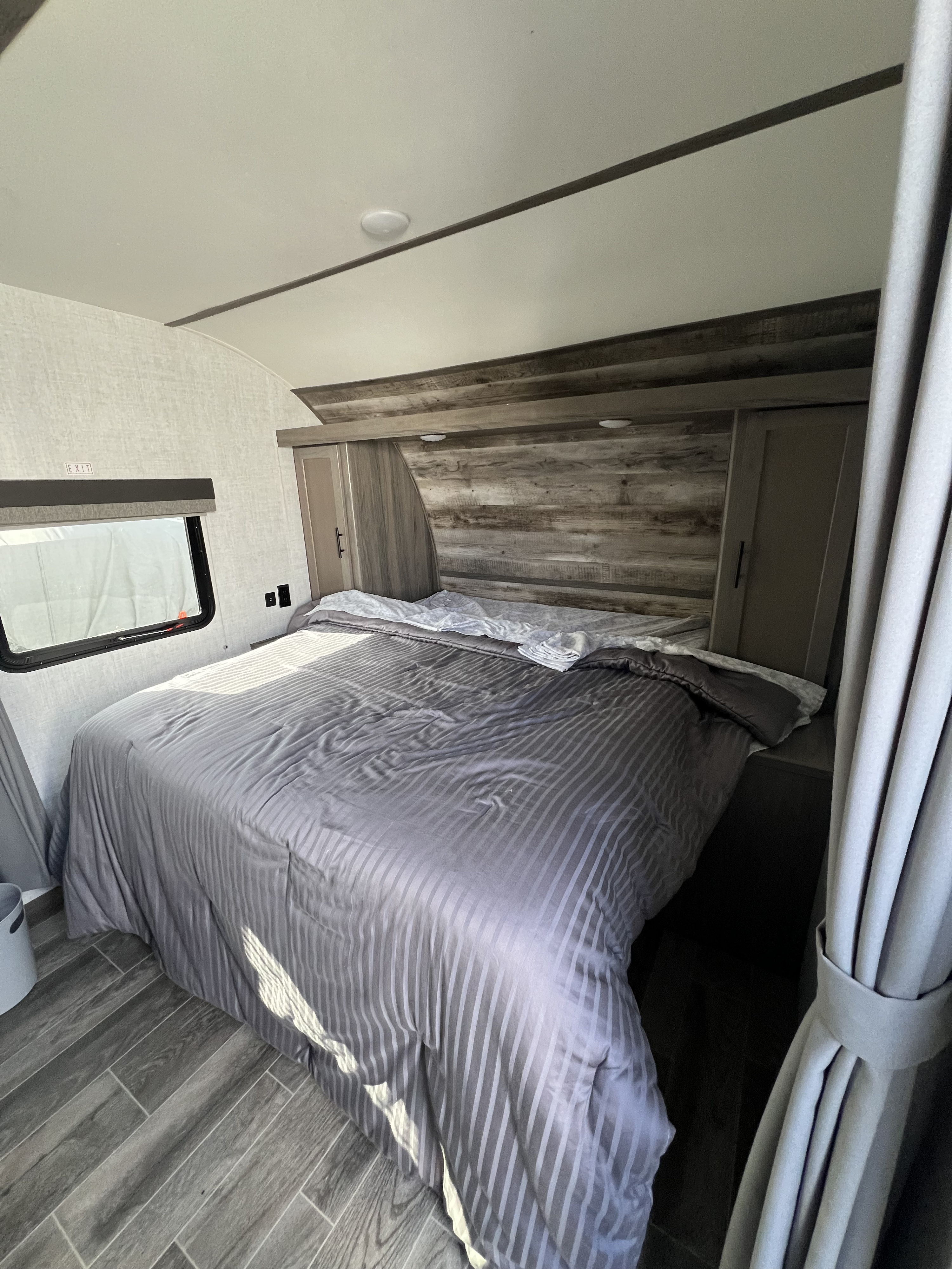 This RV rental bedroom features a comfy bed with striped bedding, wood-look headboard, storage, and an exit window.. Gulf Stream Kingsport 2021