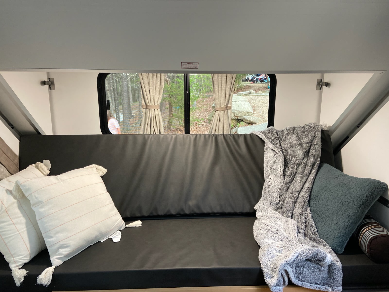 Cozy RV rental interior: black couch with white/teal pillows & gray blanket, offering a scenic campsite view.. A-Liner Ranger 2025